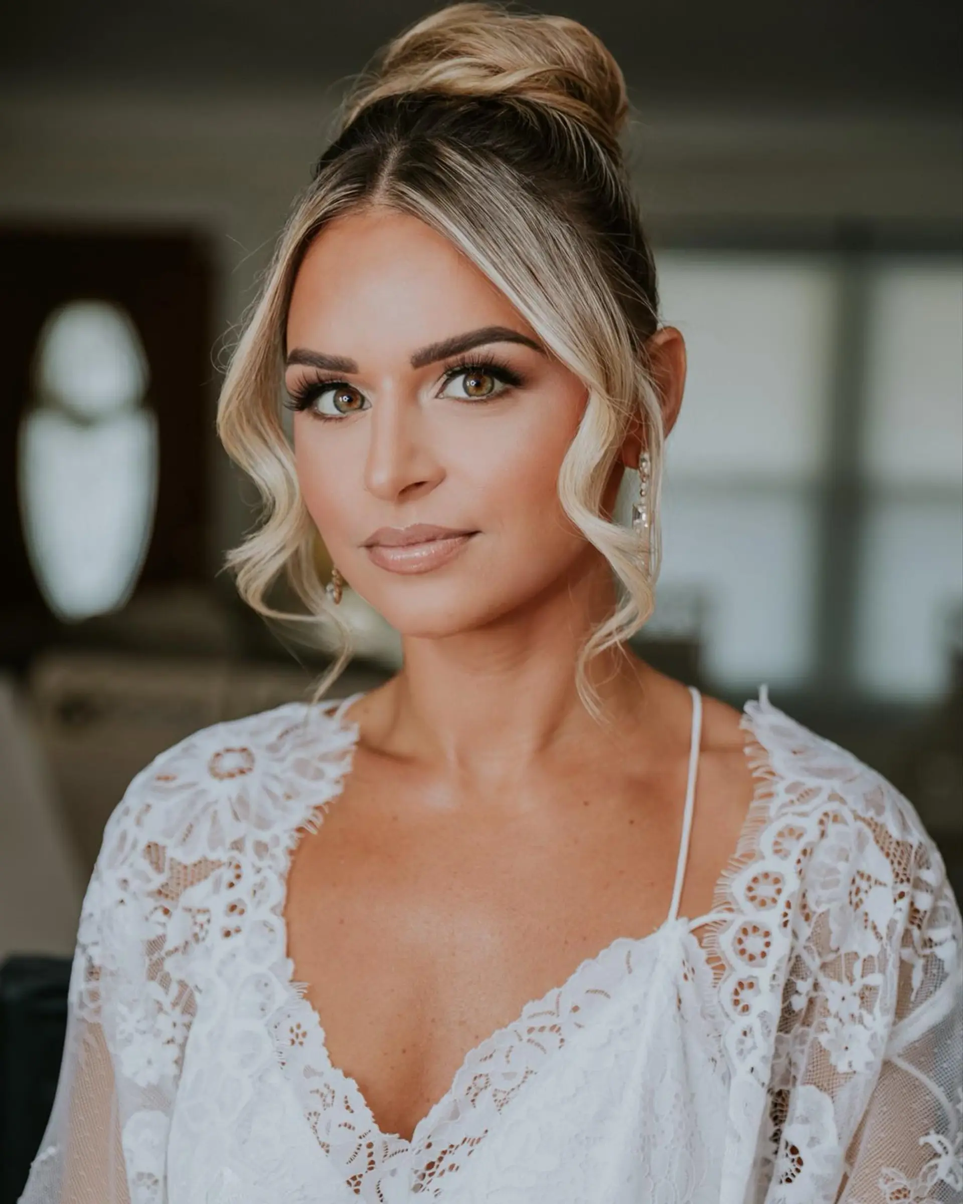 A sophisticated bridal high bun with parted, softly waved face-framing tendrils. 1