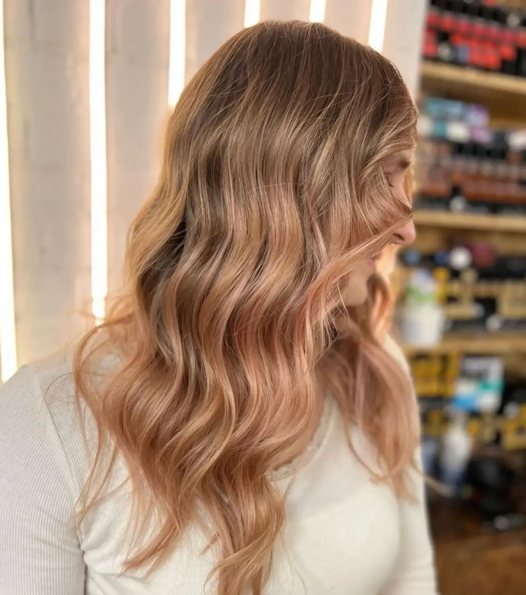 Long, wavy hair styled in cascading waves with a blend of light brown and rose gold colors. The hair falls smoothly over the shoulders with loose curls creating a beach wave effect.
