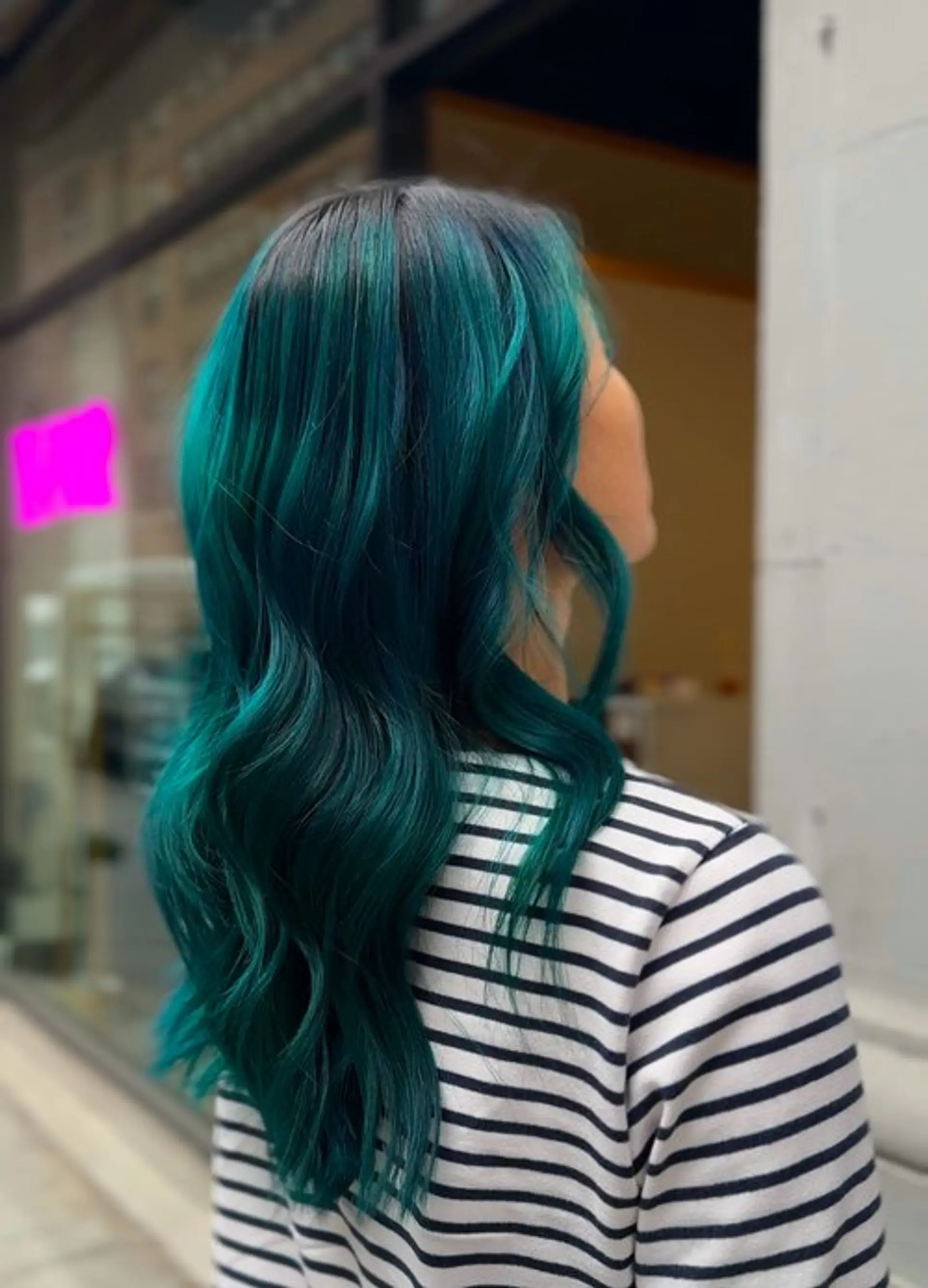 Long wavy hair with a striking teal color melt from dark roots. 1