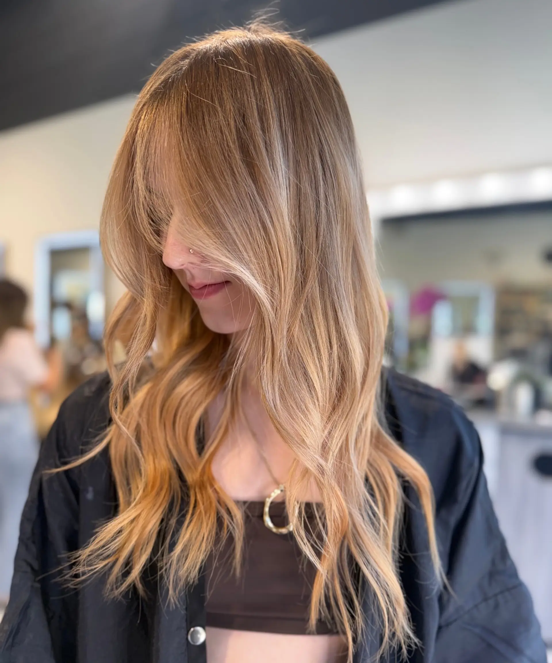 Long warm strawberry blonde hair styled in soft, flowy waves with textured, face-framing fringe. 1