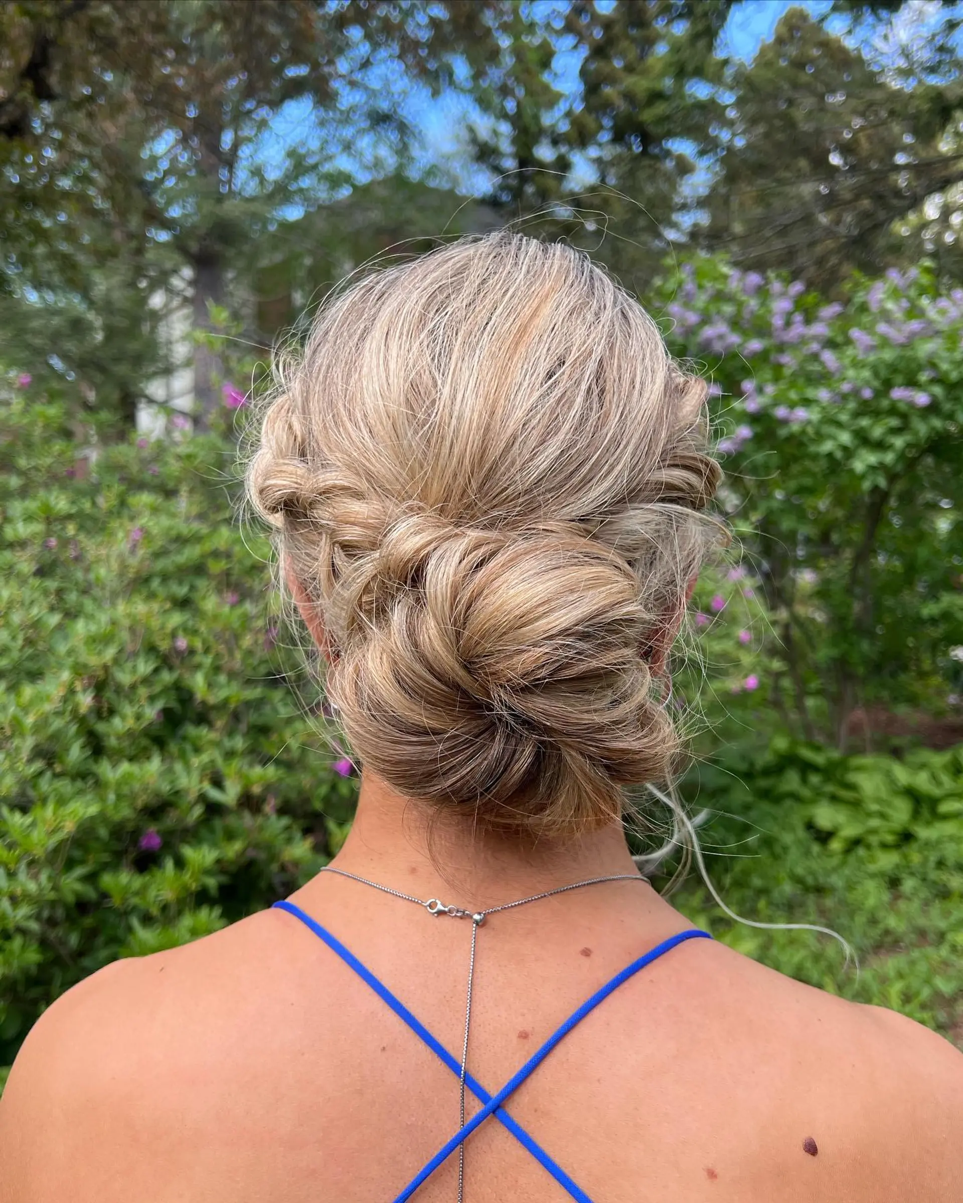 A soft, textured low bun updo with gently twisted sides, styled in dimensional highlighted blonde hair. 1