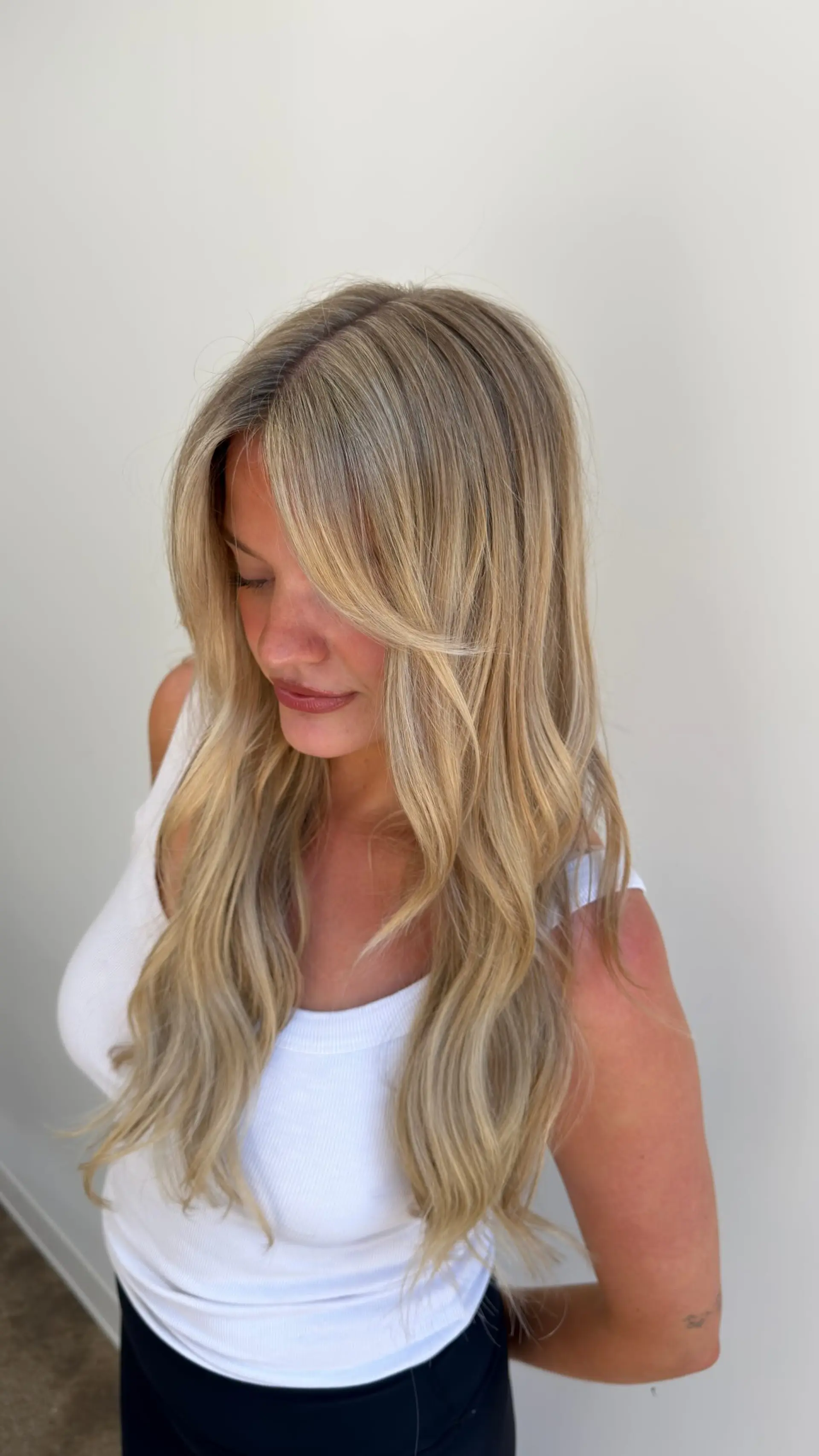 Long hair featuring dimensional blonde highlights styled into soft, relaxed waves with feathered curtain bangs. 1
