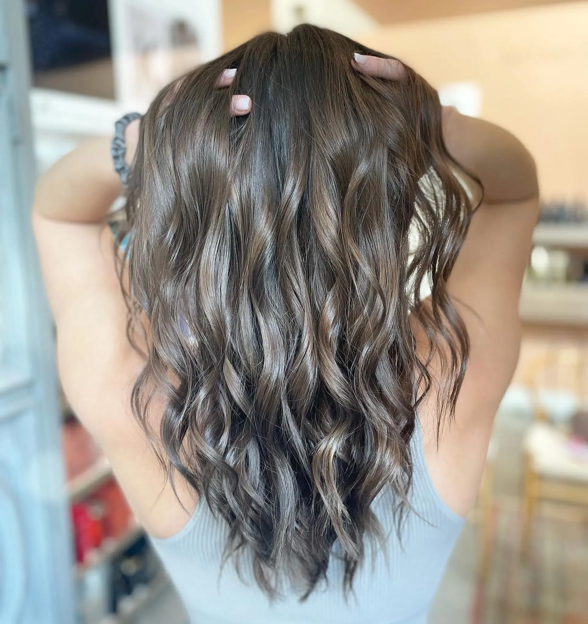 Long, glossy brunette hair styled with soft, touchable waves. 1