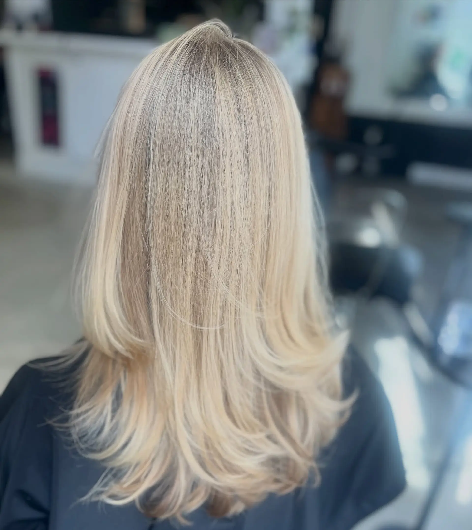 Long bright blonde hair cut into soft flowing layers with a bouncy blowout finish curving the ends outward. 1