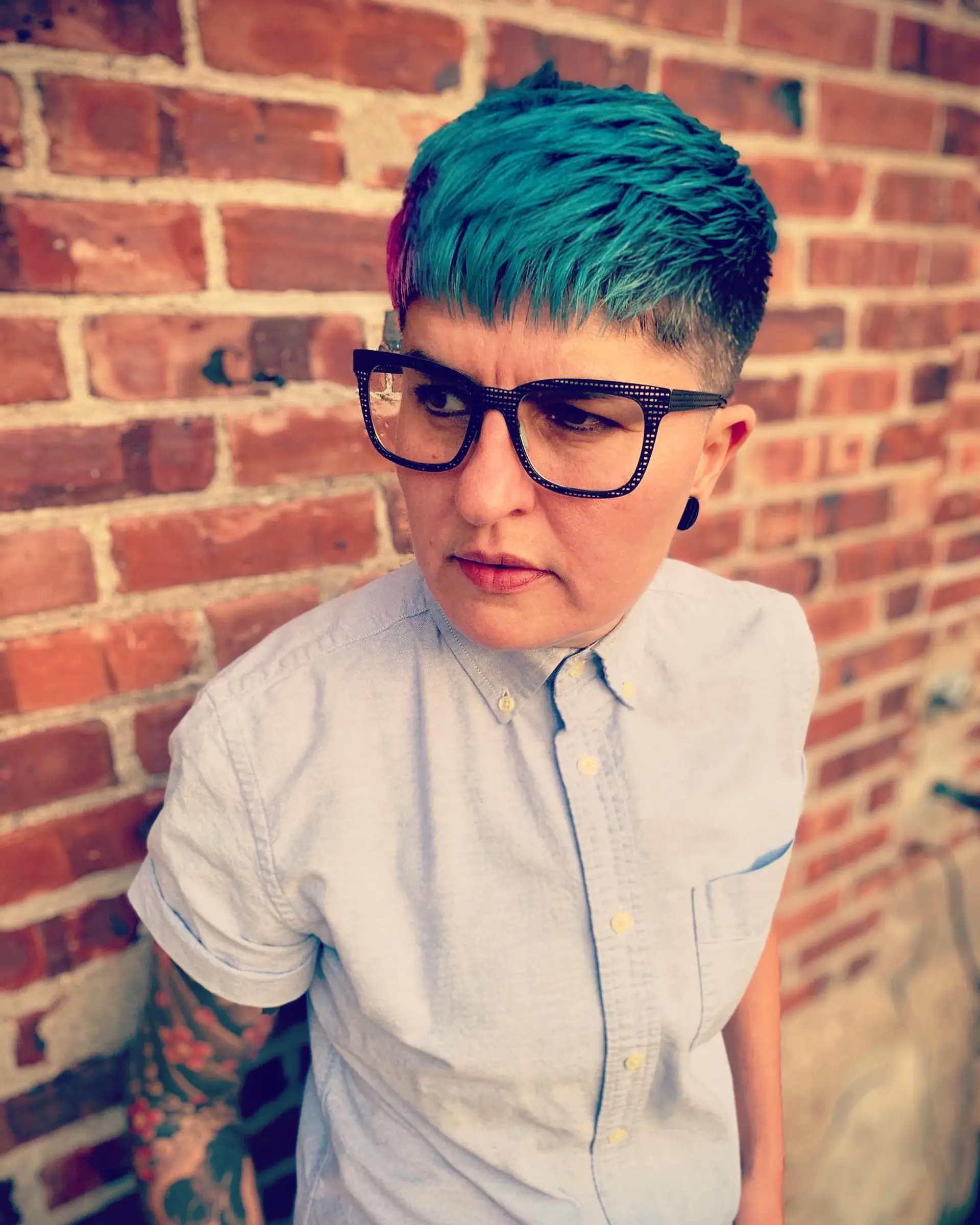 A textured short crop with faded sides and a forward-swept fringe colored in vibrant electric teal with purple accents. 1