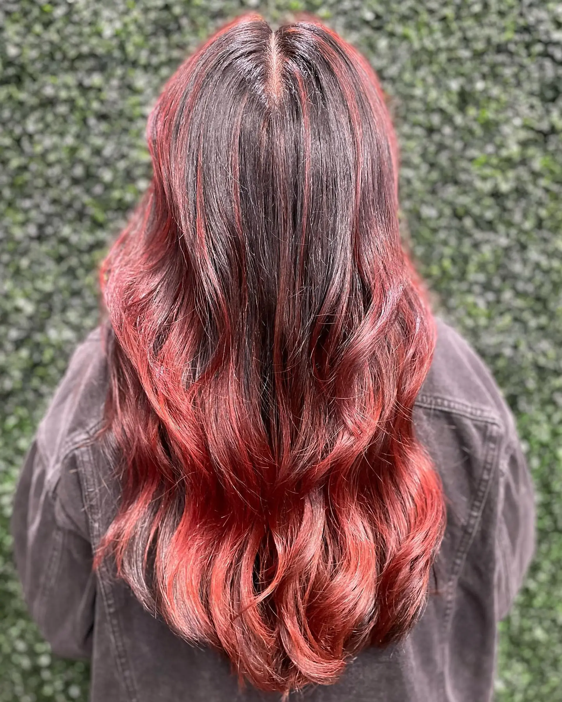 Long dark hair accented with dimensional red and copper balayage, styled in flowing loose waves. 1