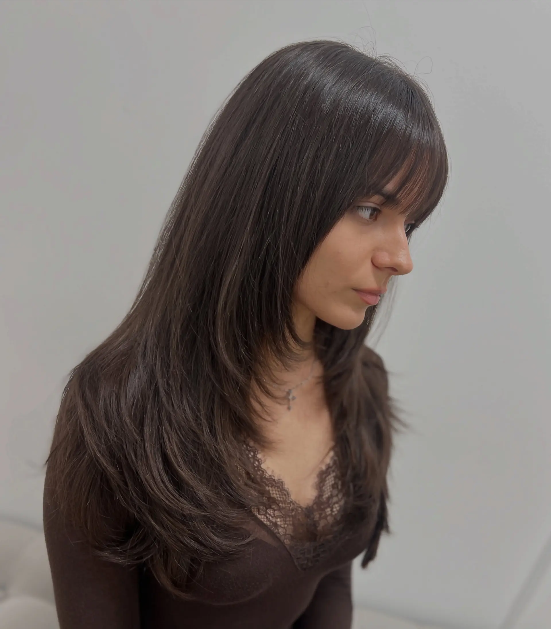 Long dark brown hair styled with soft face-framing layers and front bangs. 1