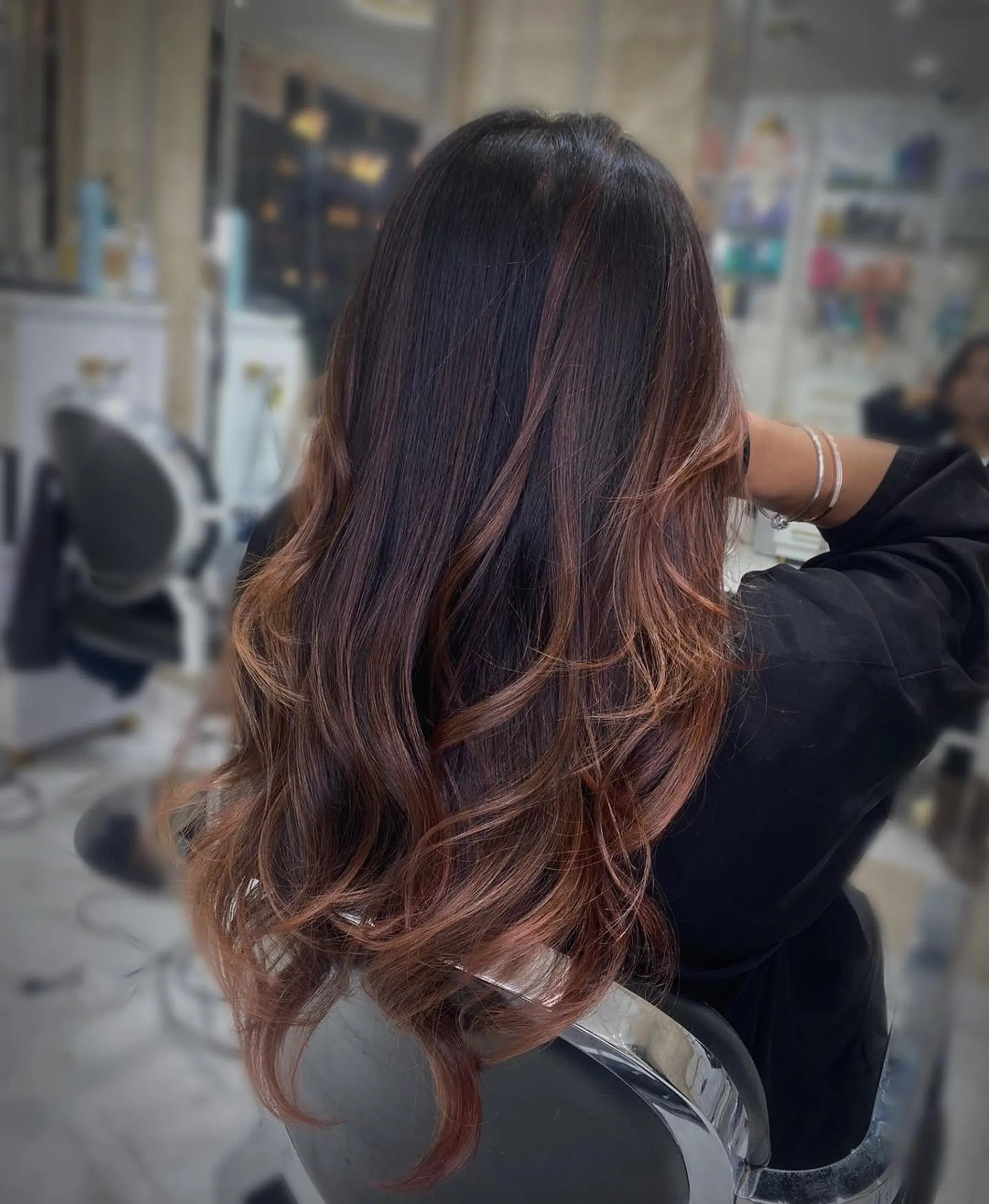 Long, wavy hair with dark brown and copper balayage, featuring layers and a glossy finish.