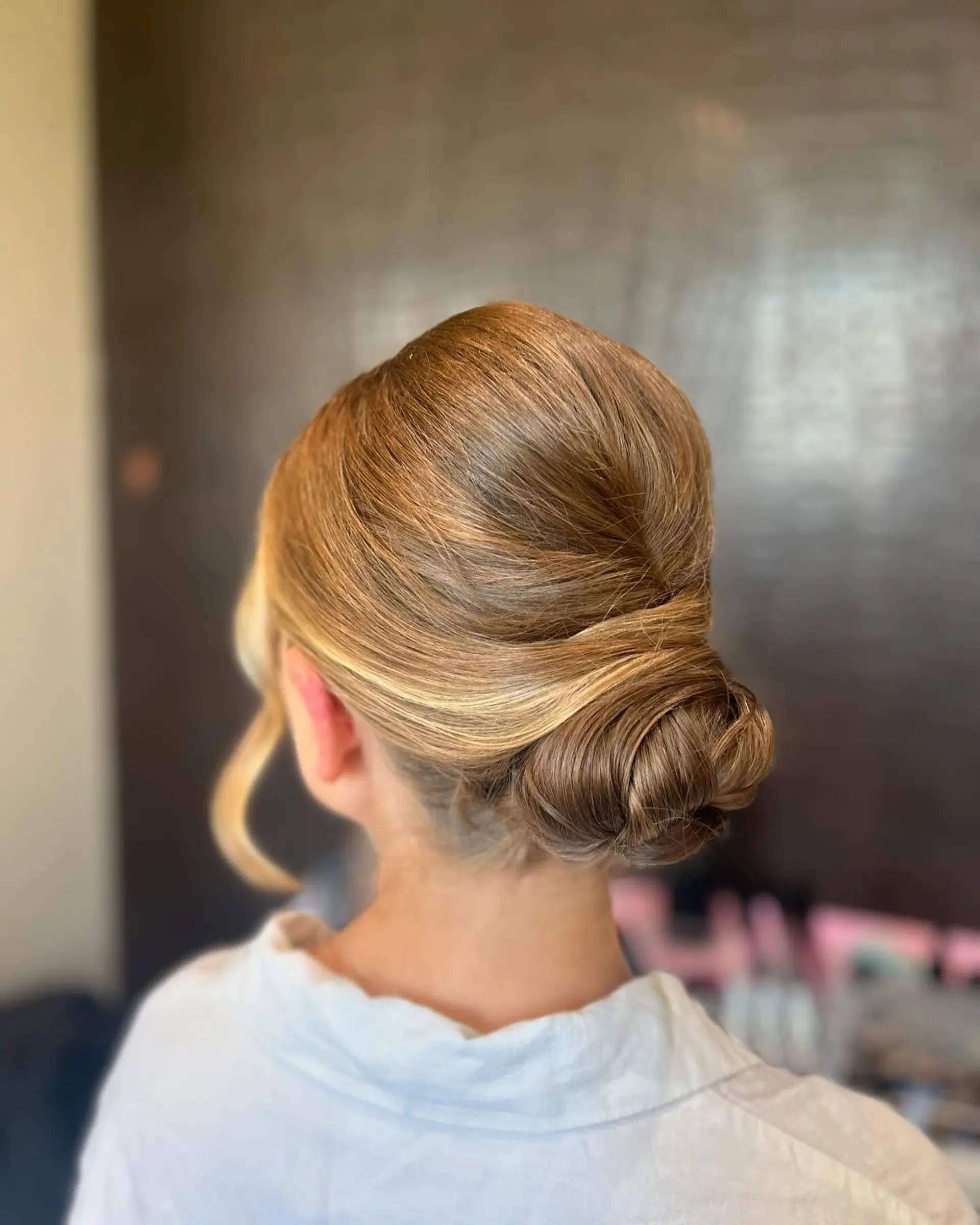 A sleek low bun bridal updo with a smooth, polished finish and soft face-framing tendrils. 1
