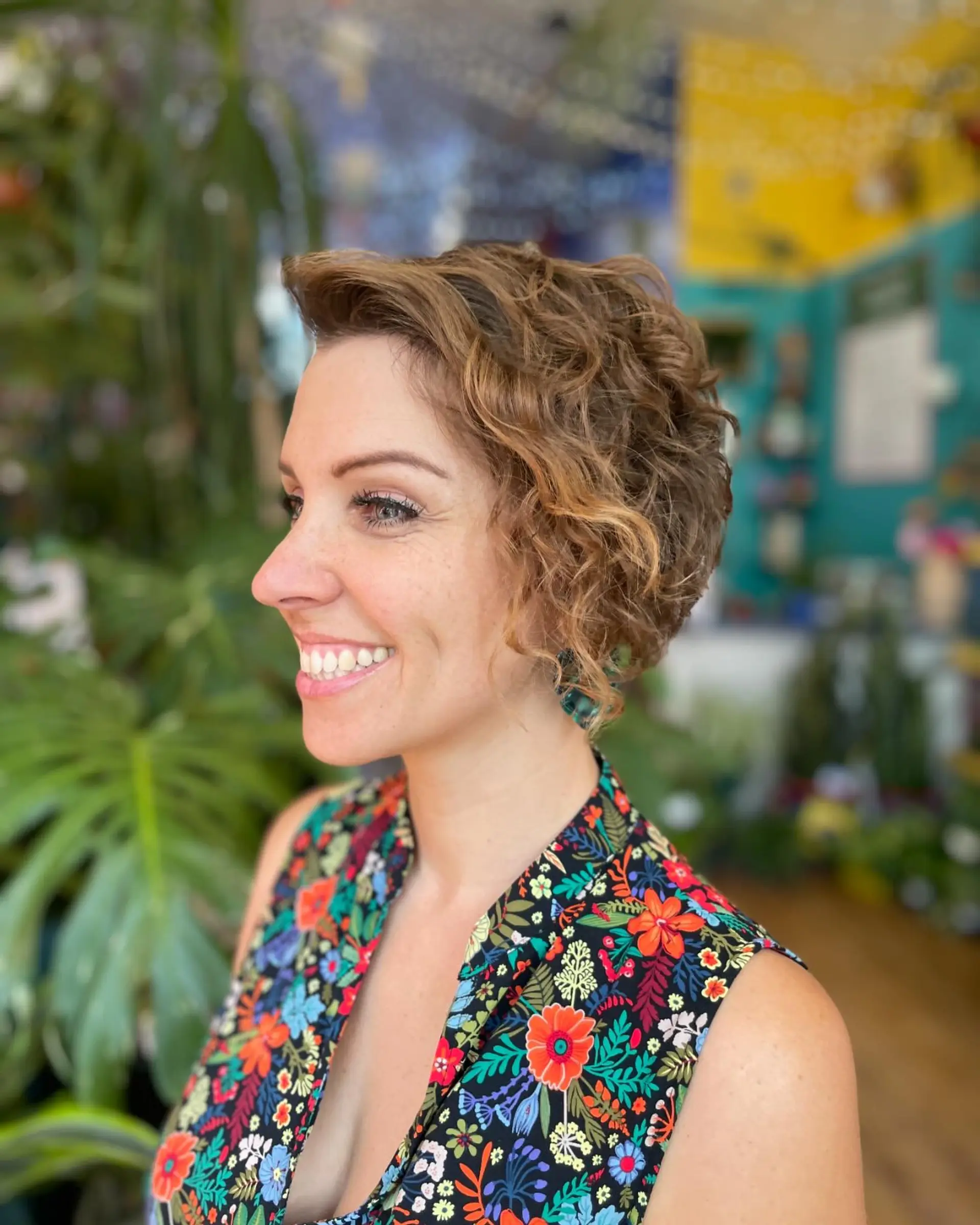 A side-swept asymmetrical short haircut styled with defined curls and subtle warm caramel highlights. 1
