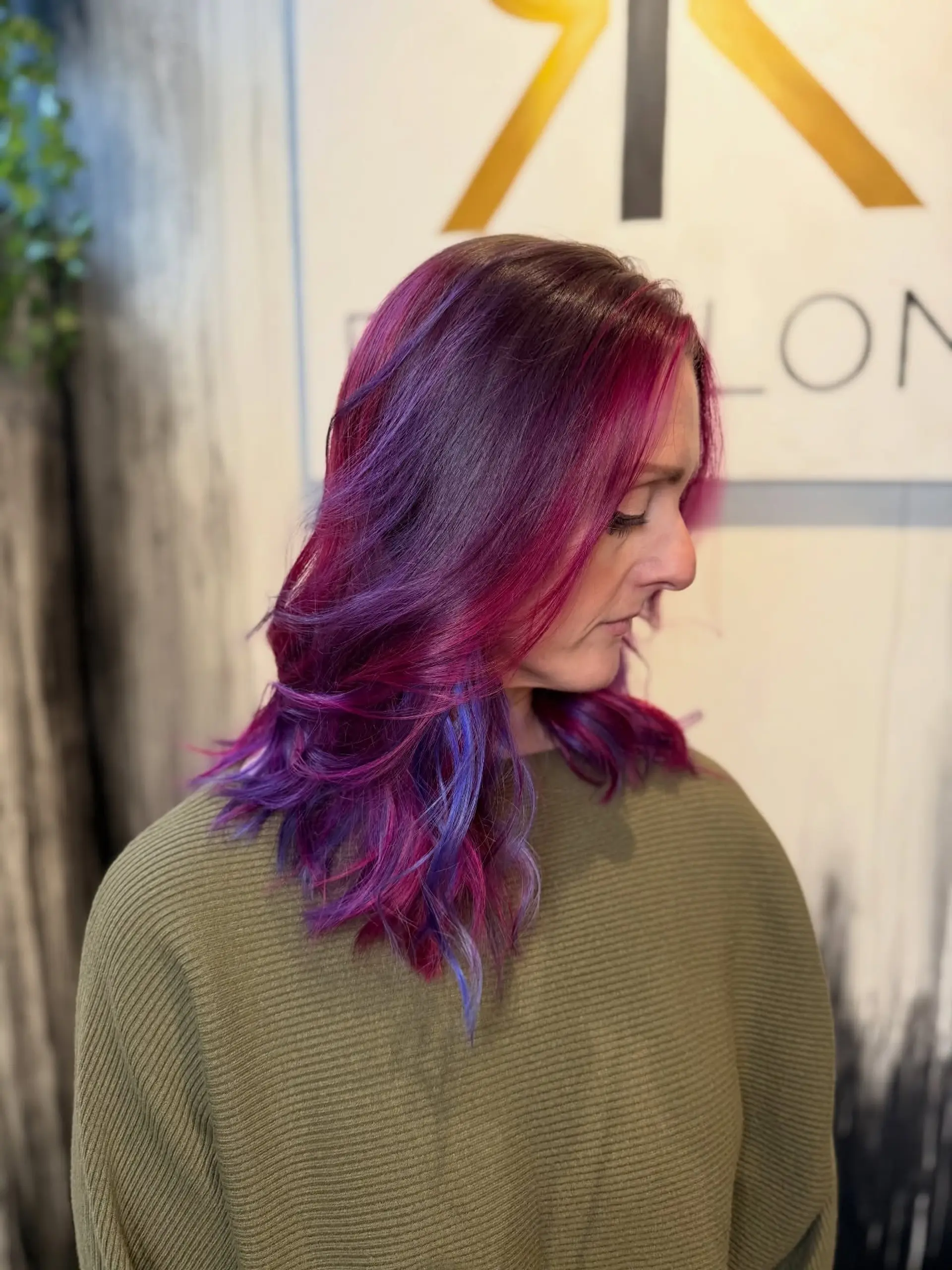 Medium-length layered hair styled in soft waves, featuring rich purple and magenta tones accented by vibrant blue peekaboo strands. 1