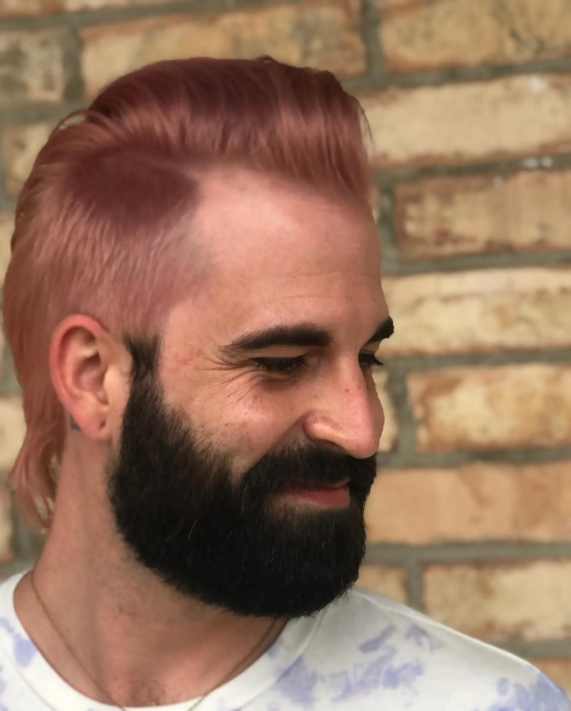 A modern mullet cut featuring short, tapered sides, length at the nape, and swept-back styling dyed in an all-over soft pastel pink. 1