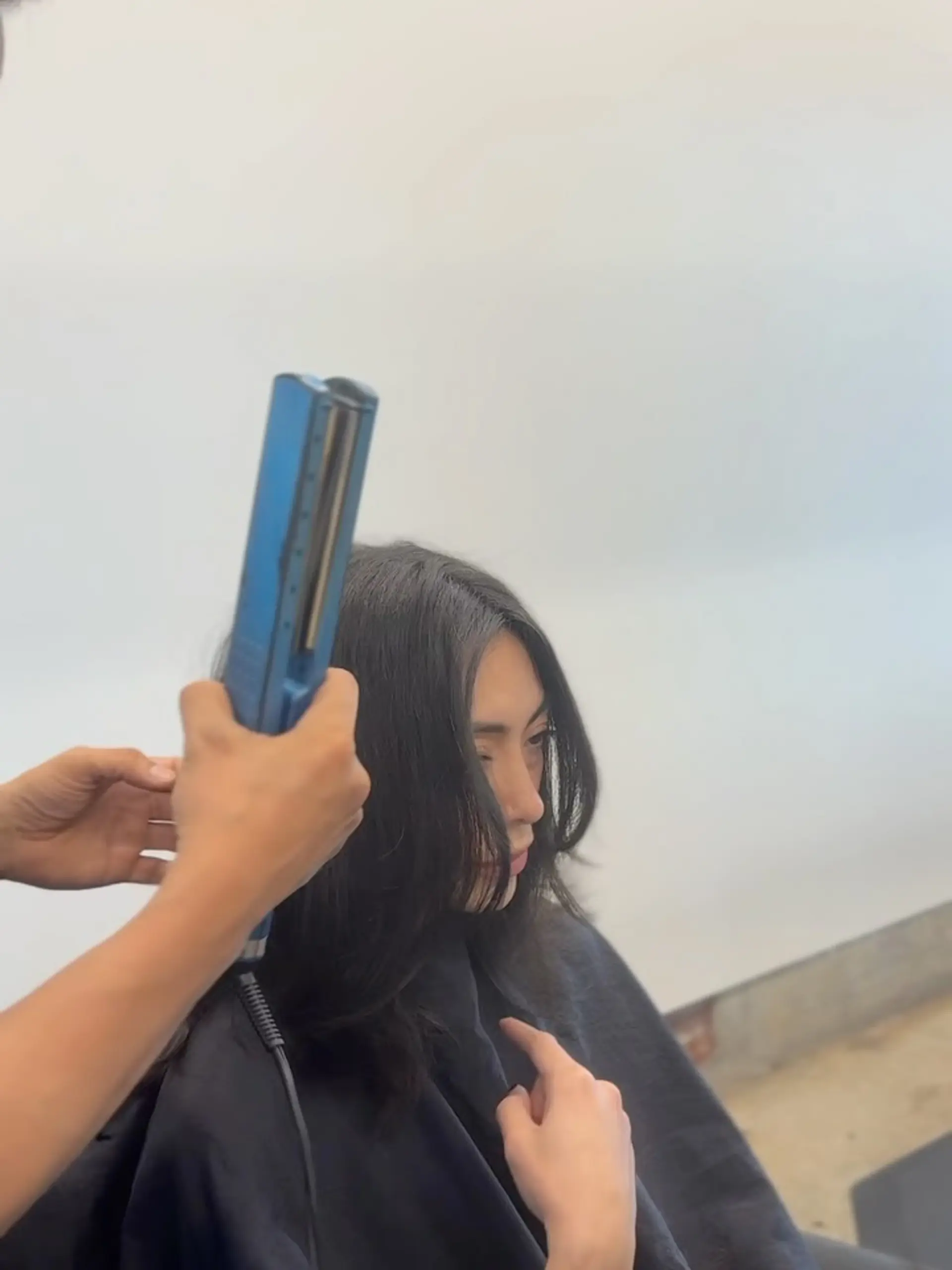 Dark, straight hair with face-framing curtain bangs and soft layers being styled with a flat iron. 1