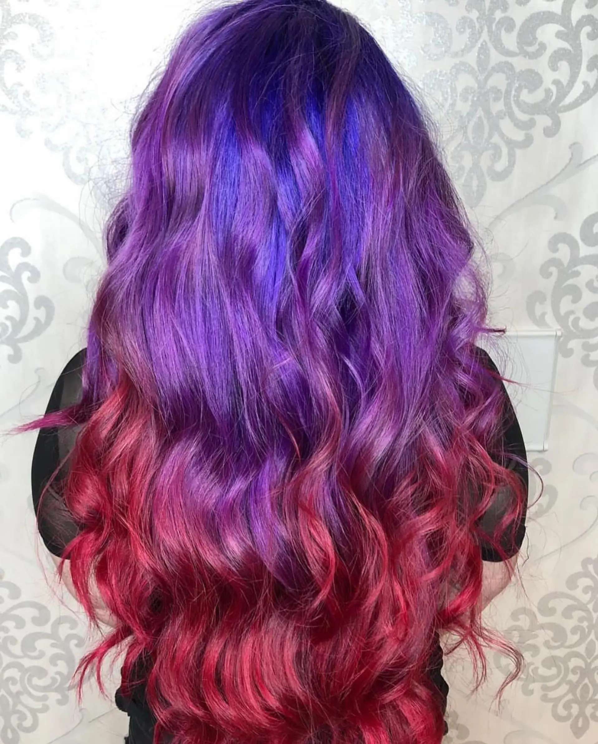 Long wavy hair featuring a seamless vibrant color melt transitioning from deep purple and violet at the roots into bright magenta and pink at the ends. 1