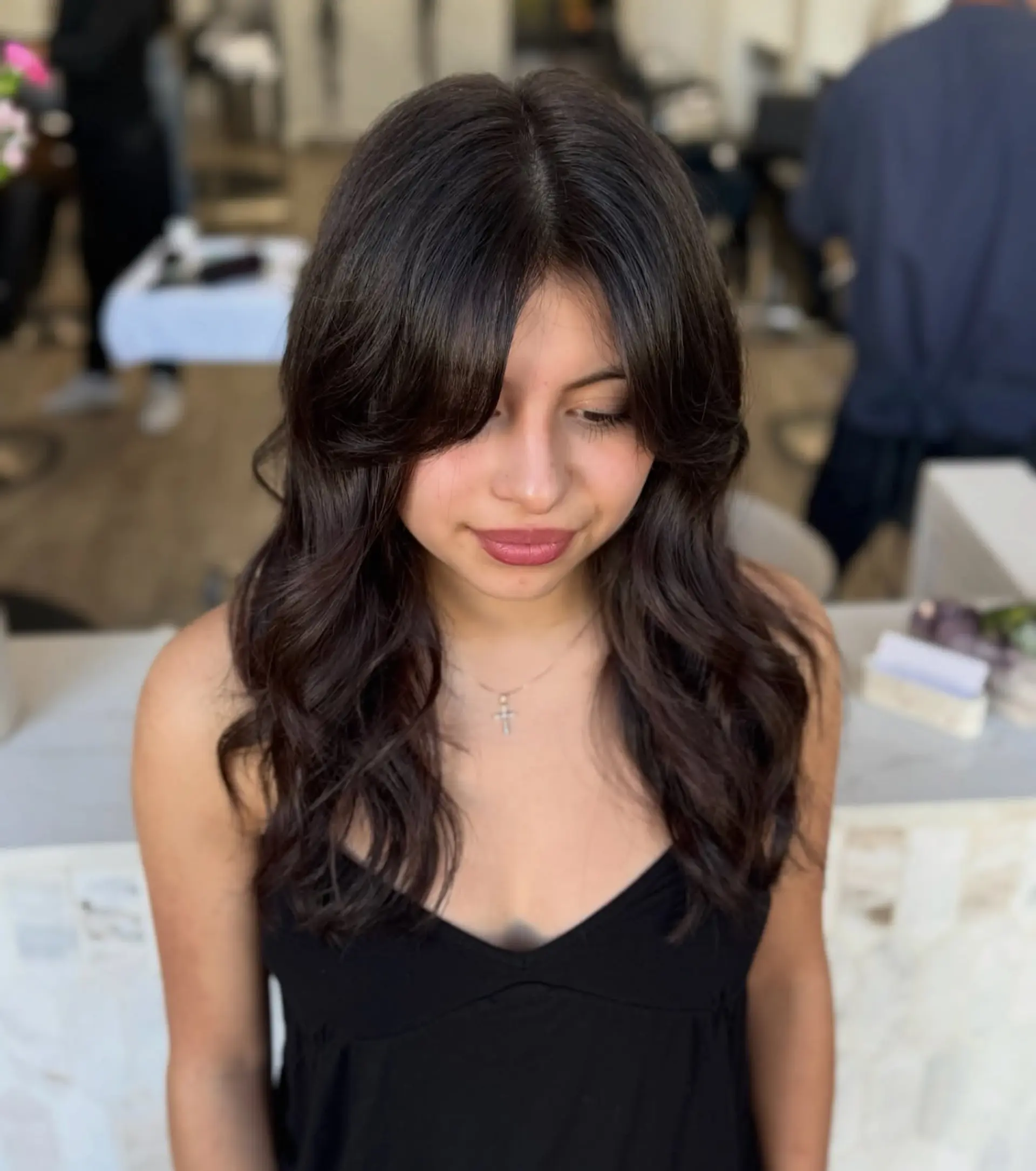 Rich dark brown long haircut featuring soft dimensional waves, layered texture, and face-framing curtain bangs. 1