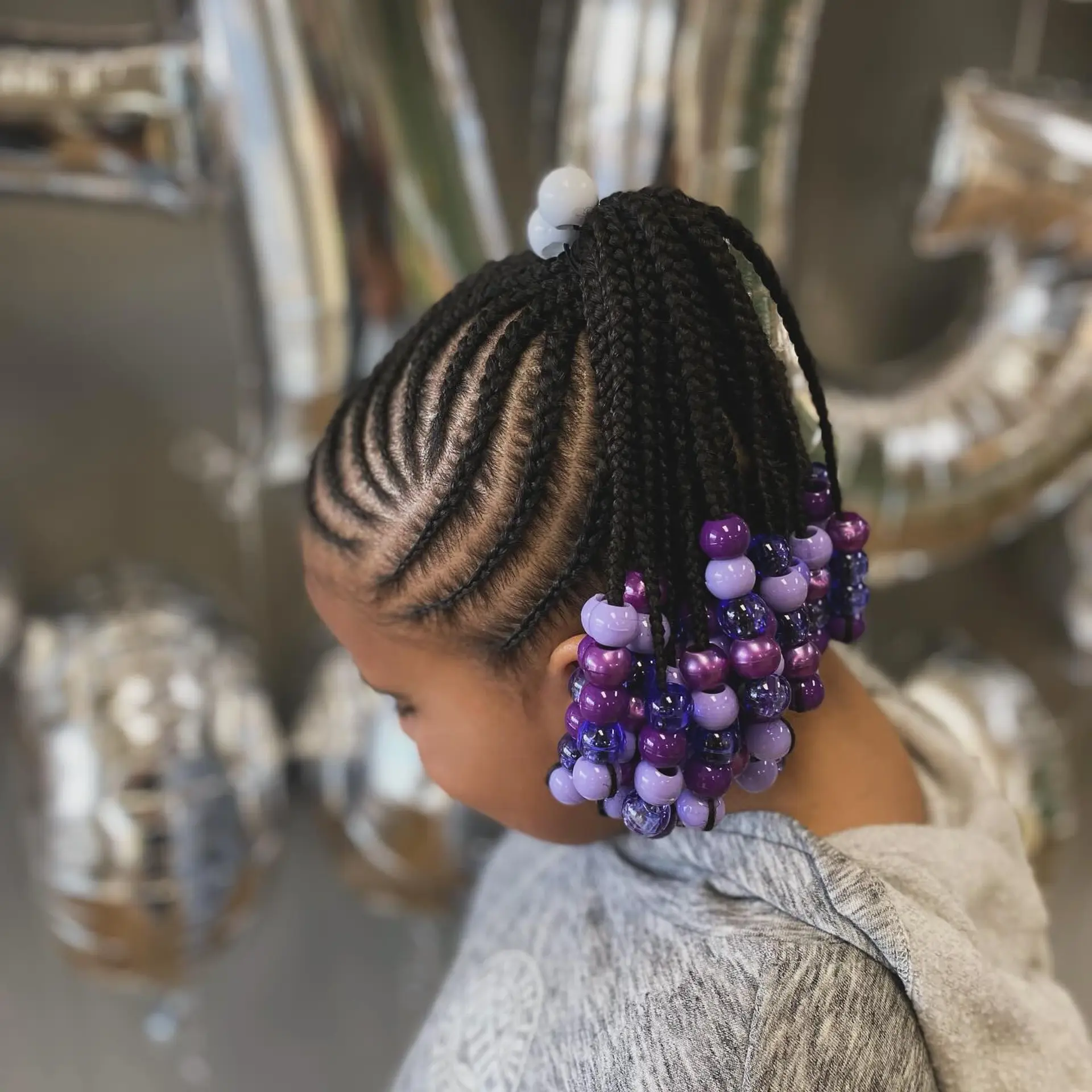 Precision cornrows braided upward into a high ponytail finished with hanging individual braids adorned with purple beads. 1