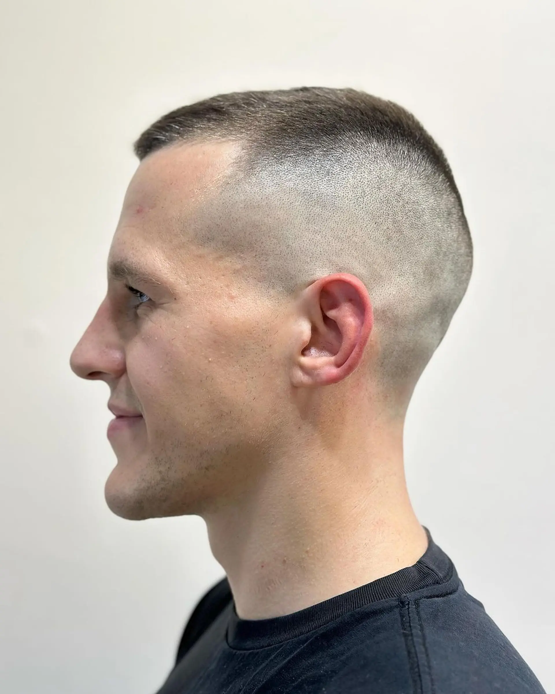 A clean-cut, very short hairstyle with tight skin fade sides and a uniformly buzzed top in dark brown. Ideal for a sleek and modern appearance with seamless transitions and clean lines. 1