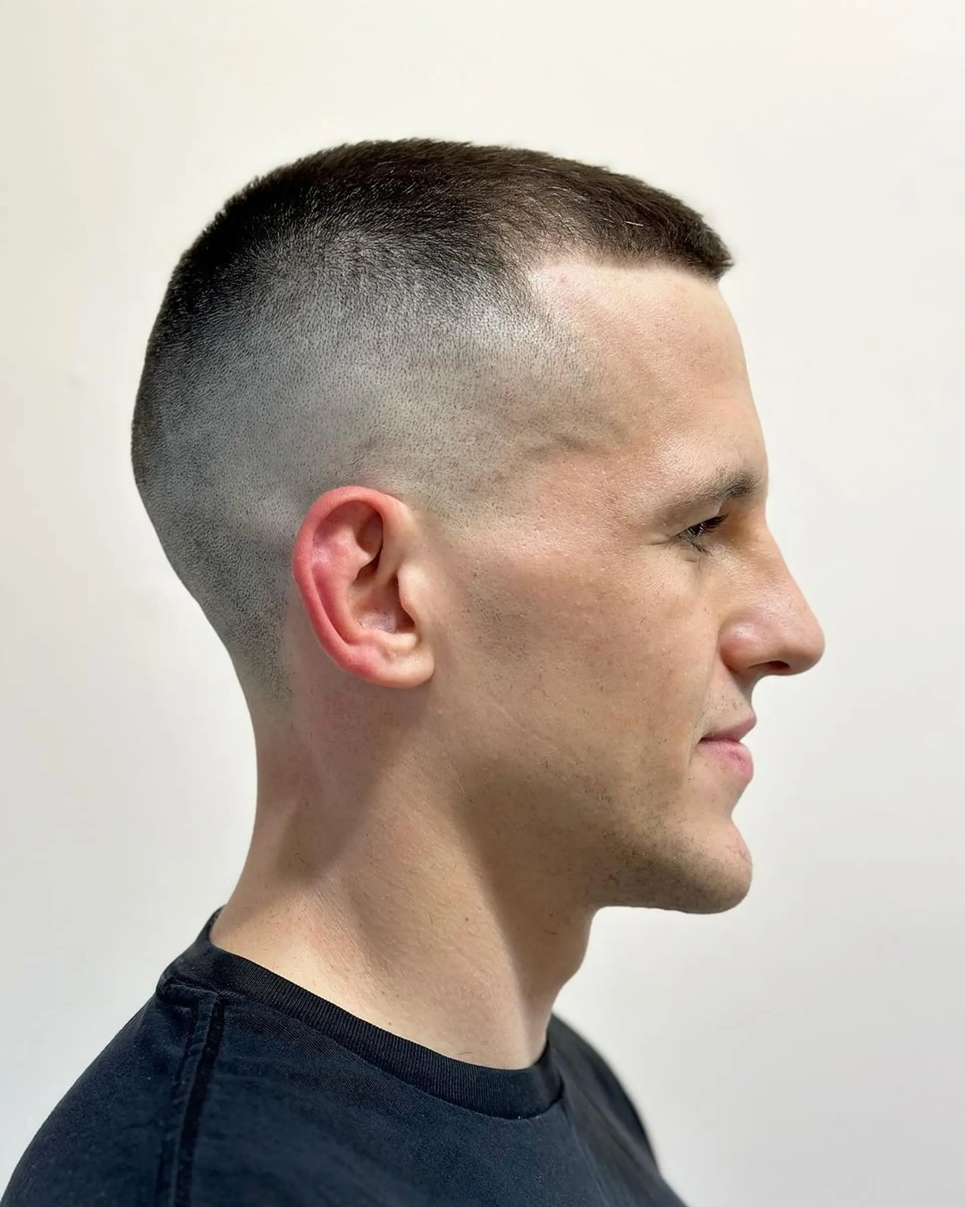 A clean-cut, very short hairstyle with tight skin fade sides and a uniformly buzzed top in dark brown. Ideal for a sleek and modern appearance with seamless transitions and clean lines. 2