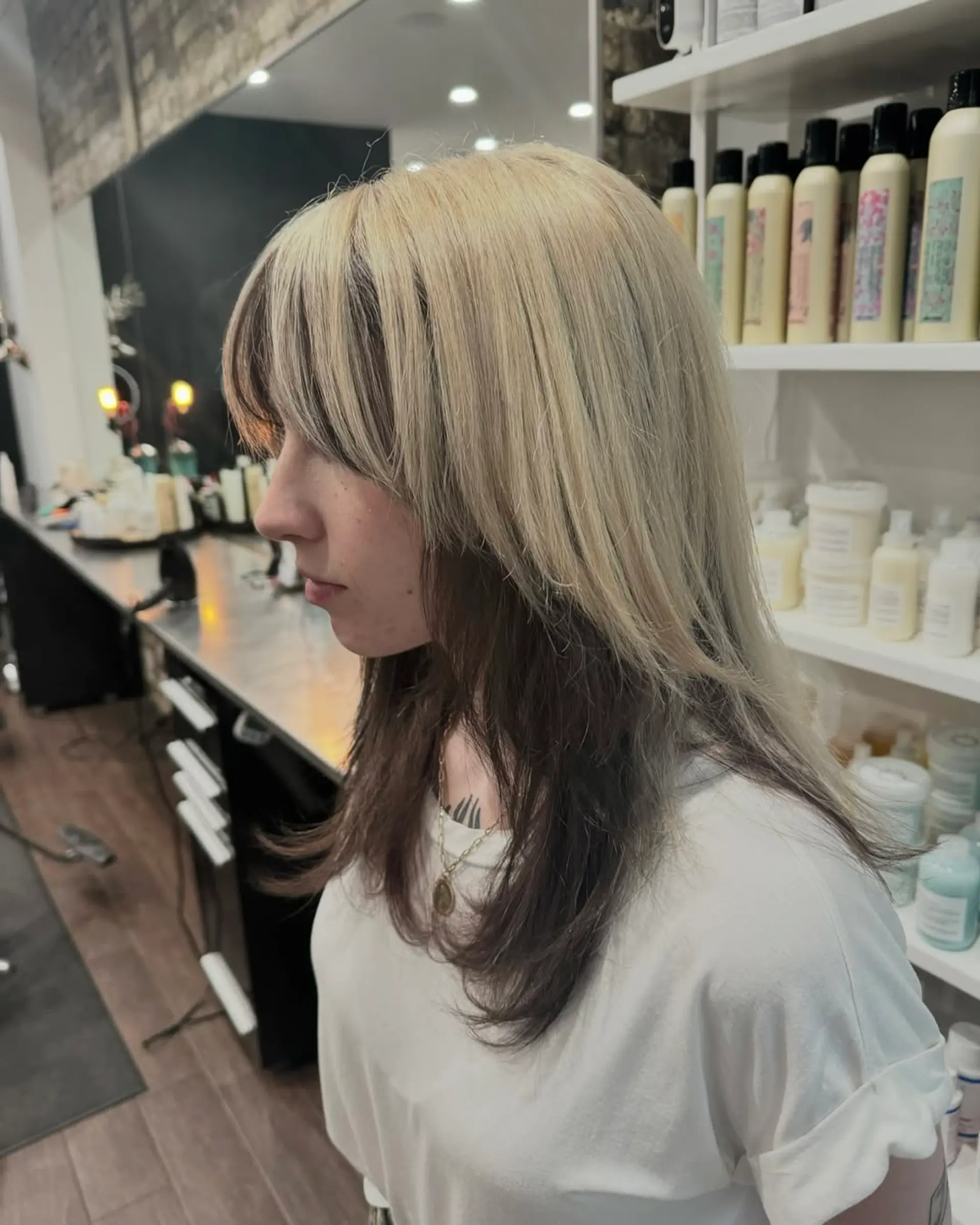 A modern shag haircut characterized by abundant choppy layers and a full, feathered fringe. The style is distinguished by a striking two-tone color, featuring a bright platinum blonde on the top layers and a dark brunette on the underside, creating a strong contrast and dynamic depth. 1