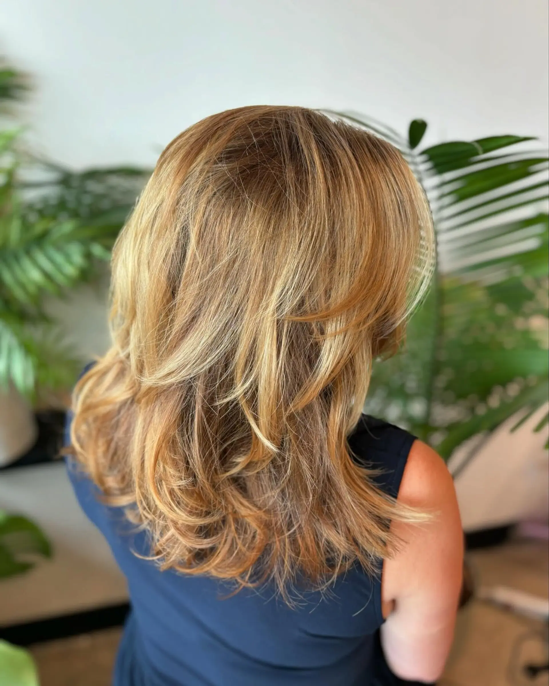 Medium-length haircut with face-framing layers and soft flicked ends, highlighted with warm golden blonde balayage. 1