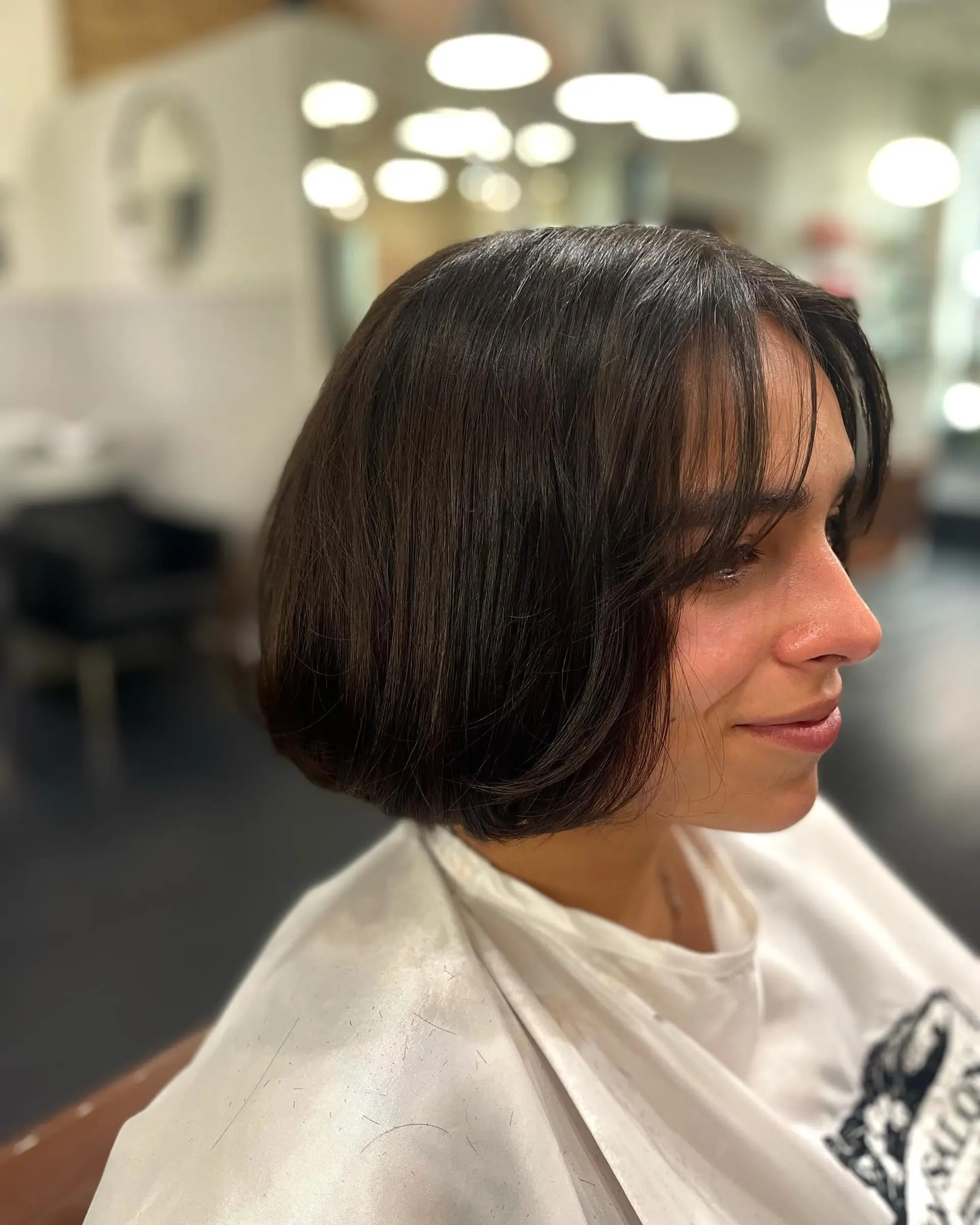 A chic chin-length French bob featuring softly tucked ends and lightweight, parted wispy bangs in a rich dark espresso brunette. 1