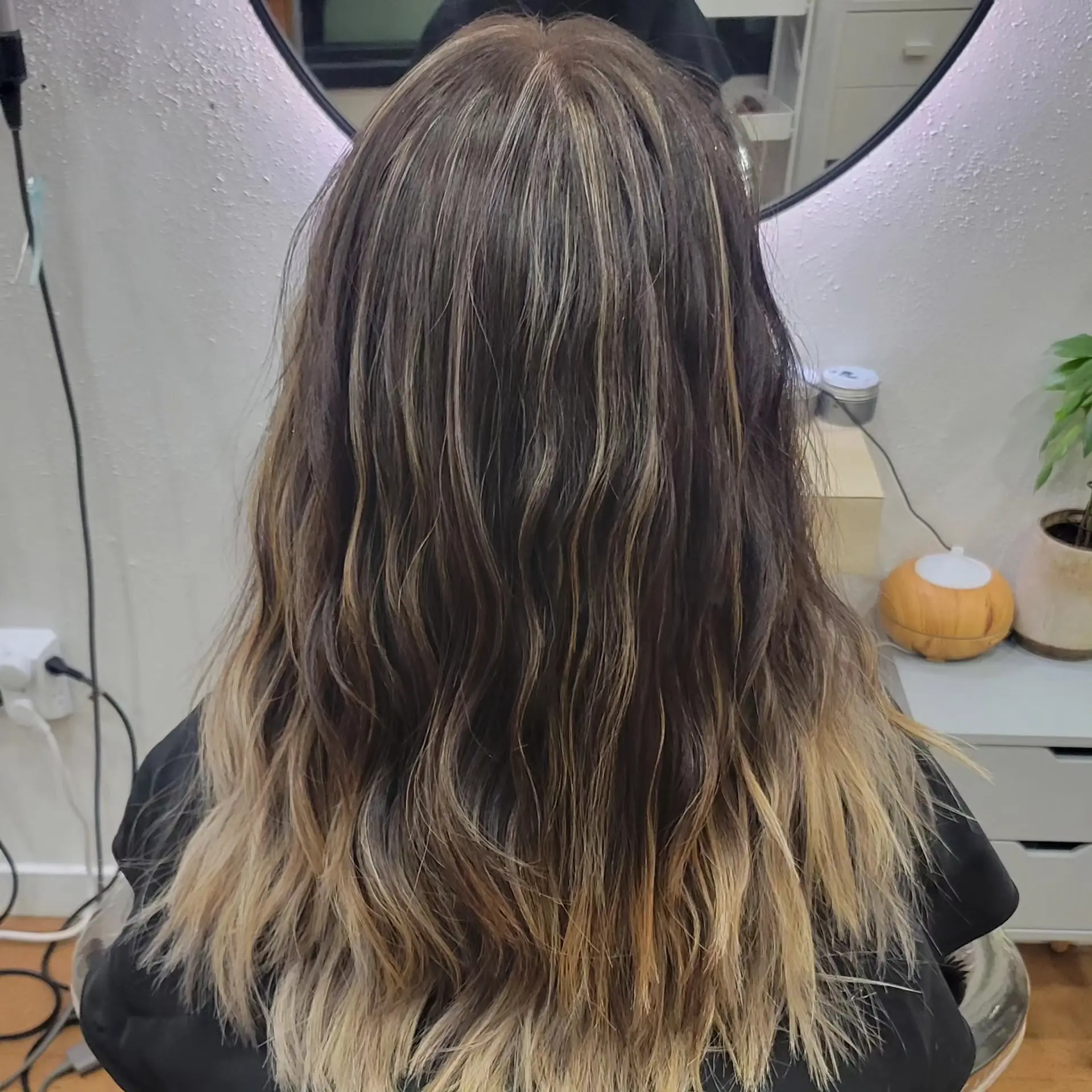 Long dark brown hair enhanced with blended balayage highlights fading into lighter blonde ends, styled with loose textured waves. 1