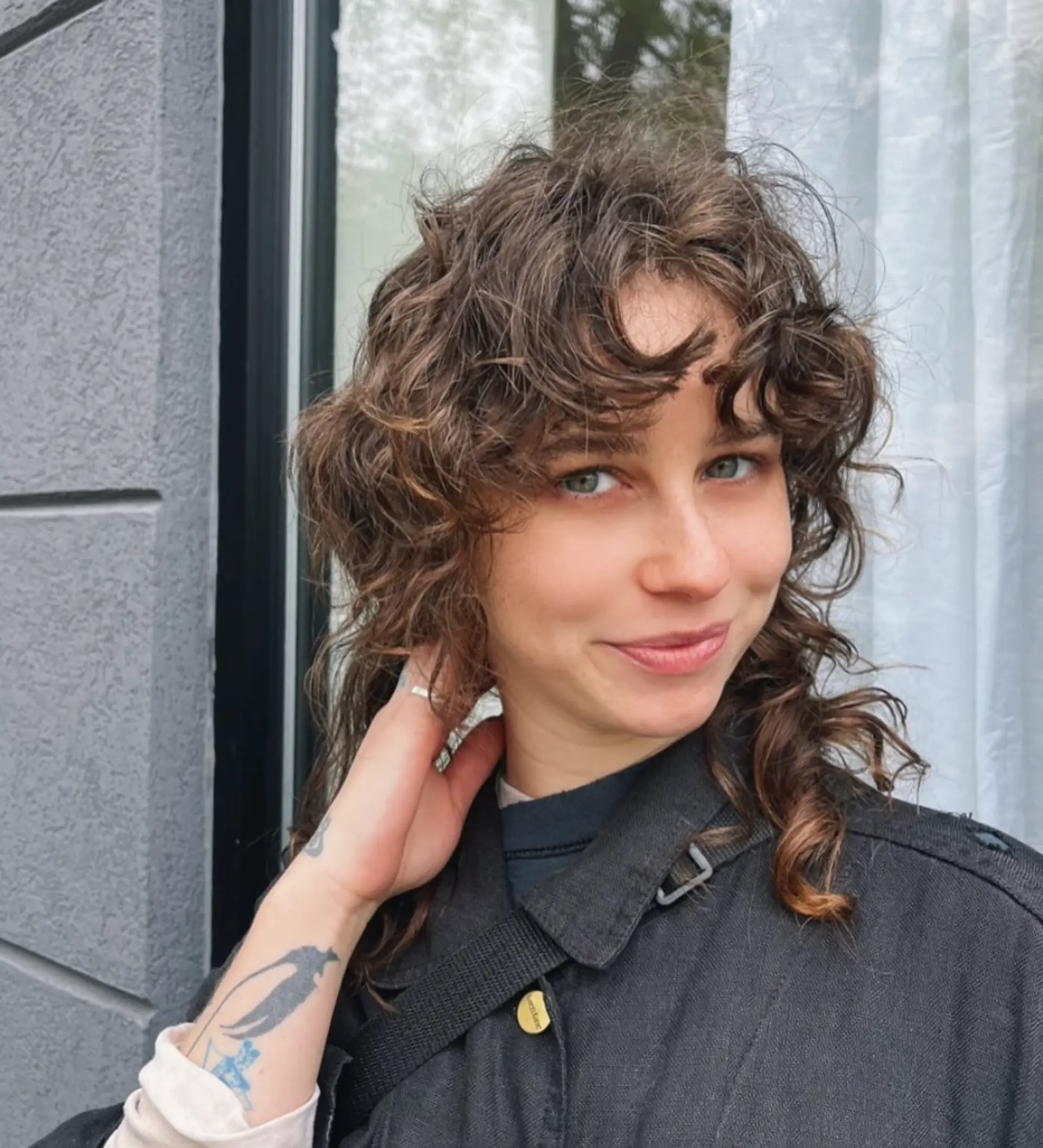 A medium-length, curly hairstyle in a brown hue with voluminous curls and curly bangs framing the face, accentuating a natural, bohemian texture.

Stylist: @reina_hair_ny
 1