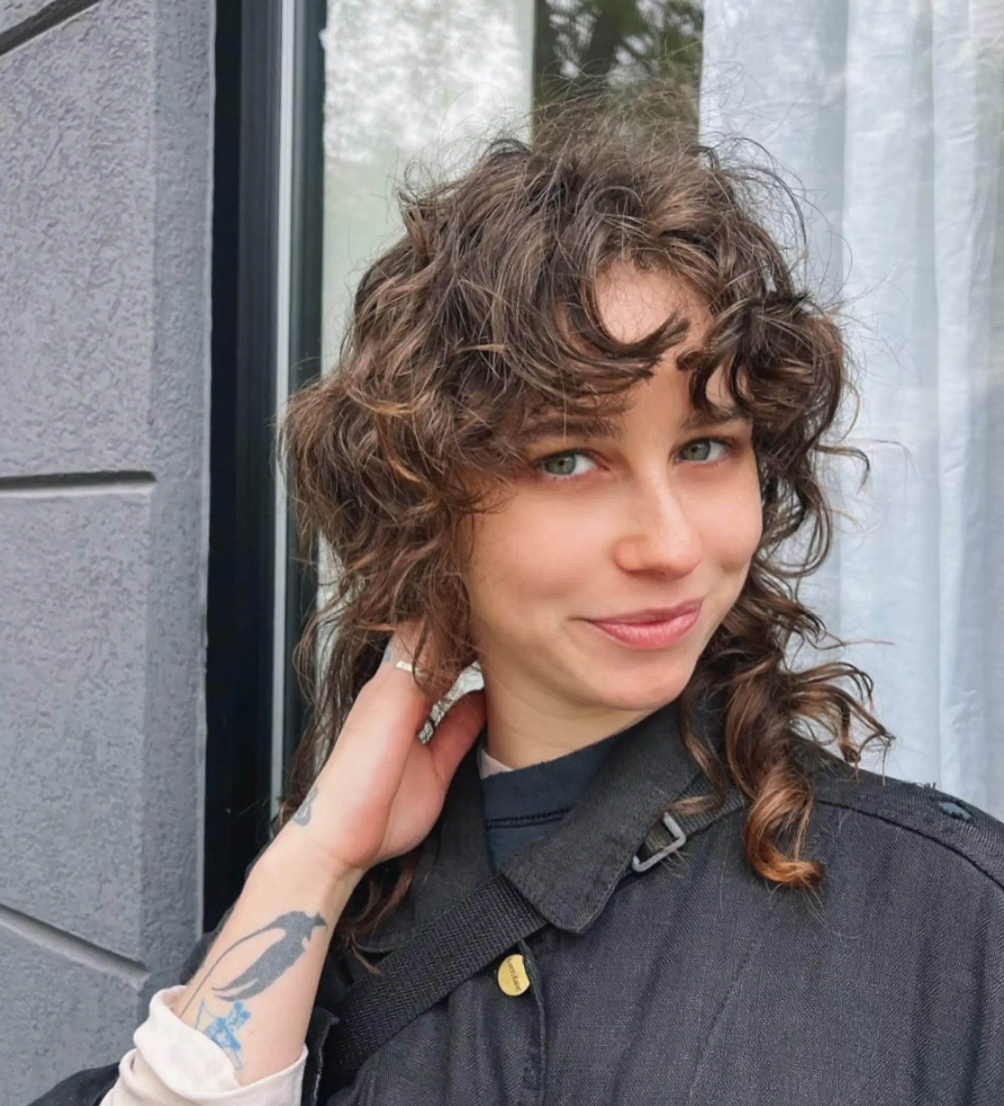 A medium-length, curly hairstyle in a brown hue with voluminous curls and curly bangs framing the face, accentuating a natural, bohemian texture.

Stylist: @reina_hair_ny
