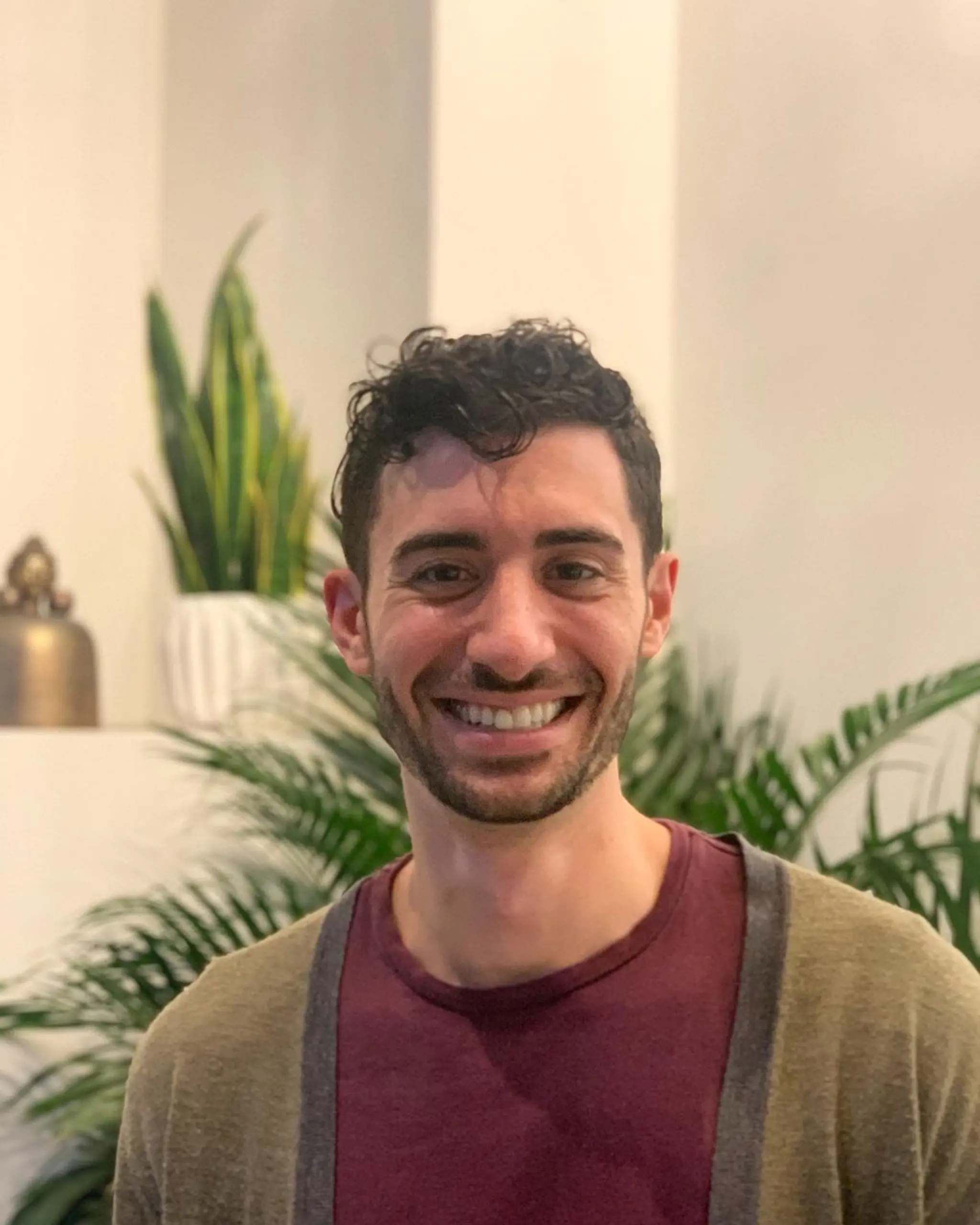 A naturally curly, short-length hairstyle featuring textured black curls with longer length and volume on top and shorter sides.