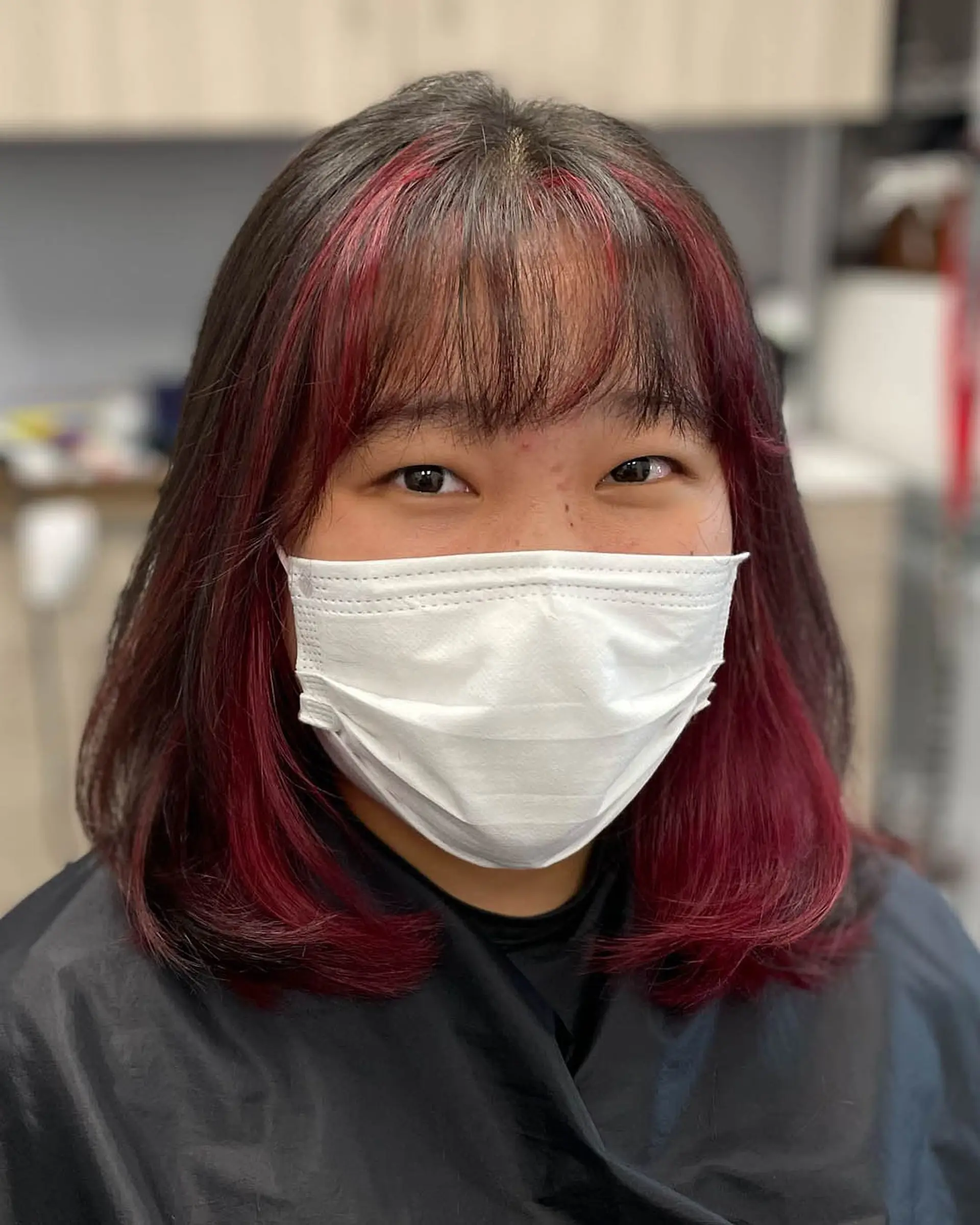 A medium-length lob featuring wispy textured bangs and vibrant burgundy face-framing color. 1