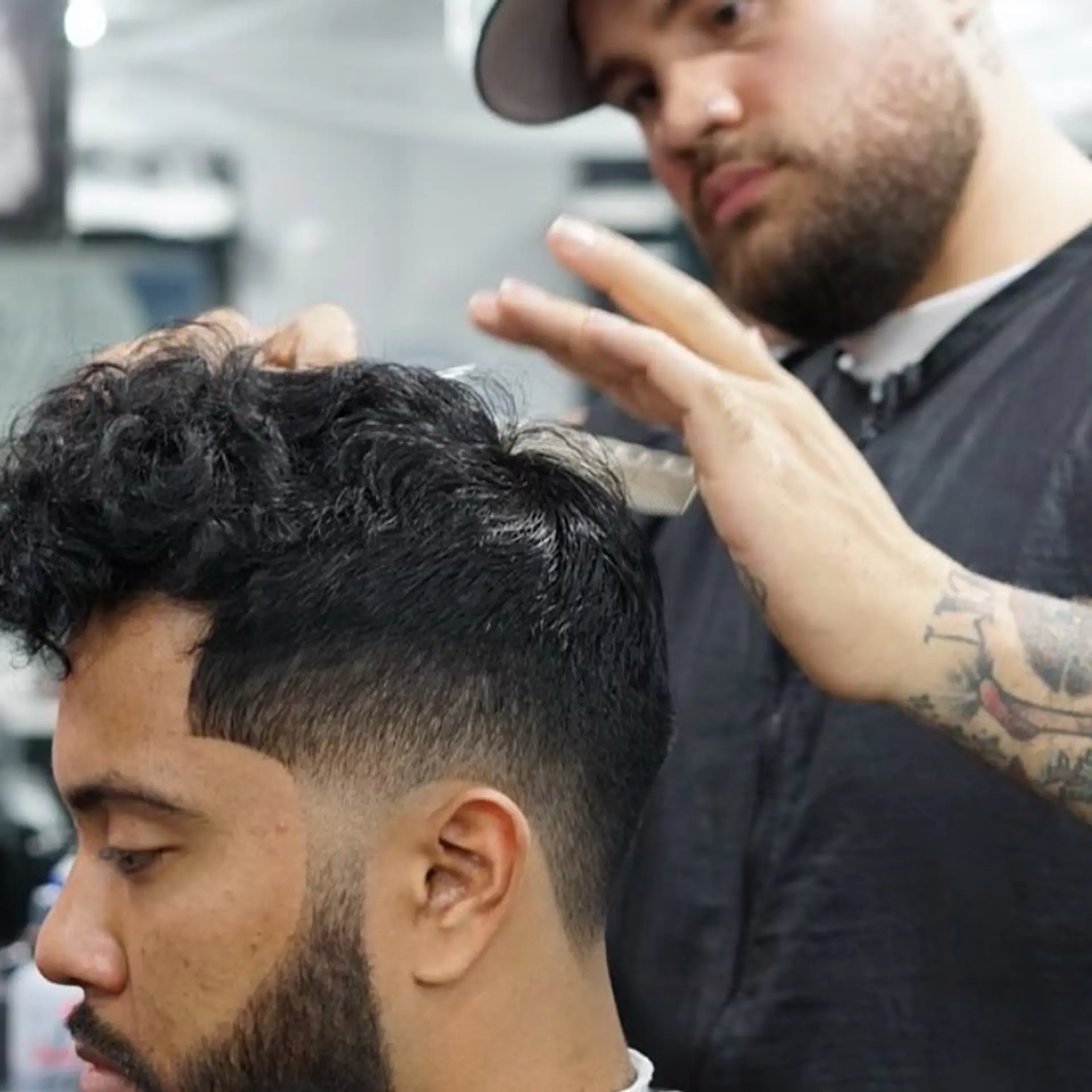 A sharp low taper fade paired with natural textured curls on top and a crisp edge-up connecting to a groomed beard. 1