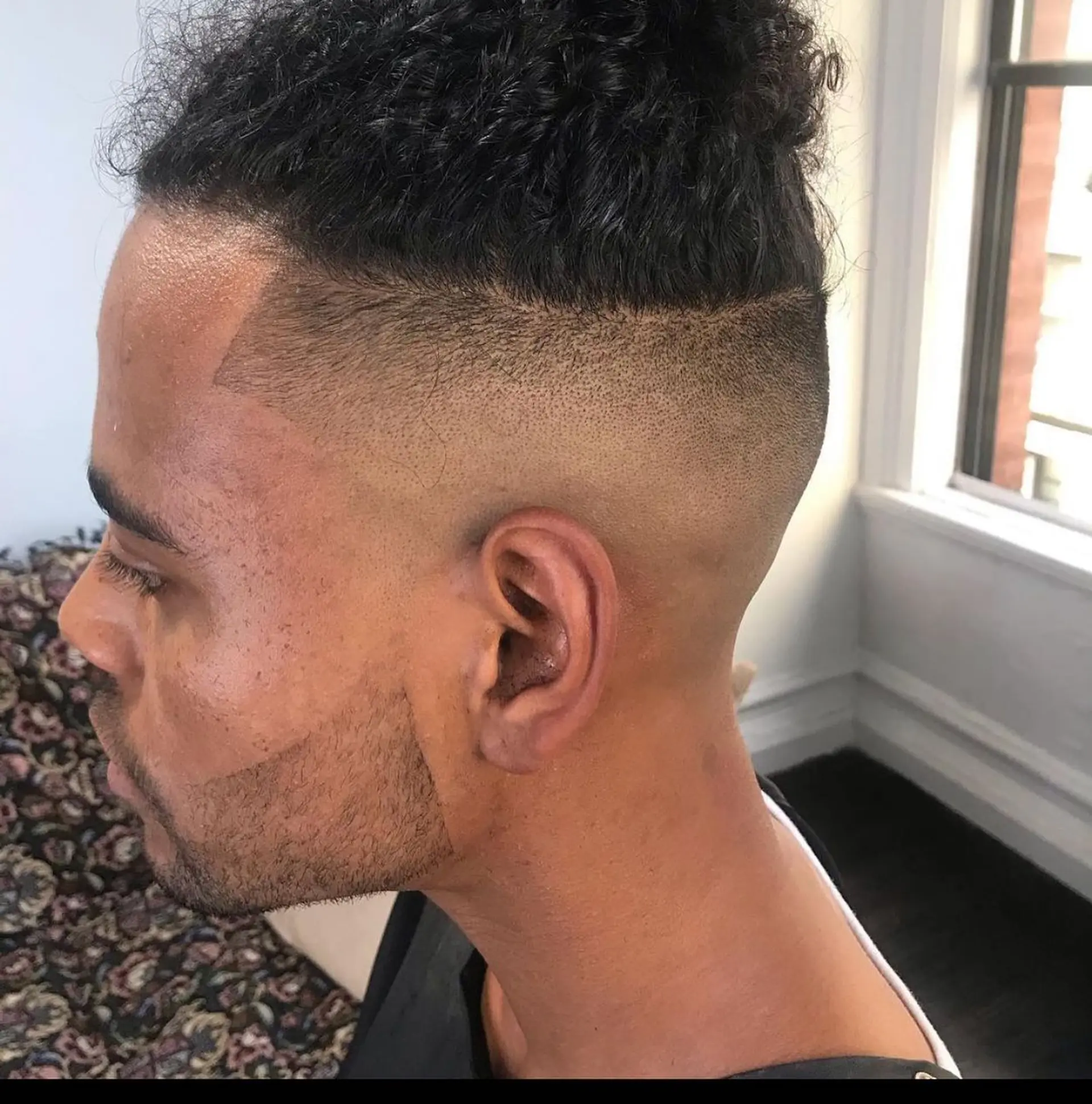 A high bald skin fade with a sharp edge-up and defined beard line, paired with curly textured hair on top. 1