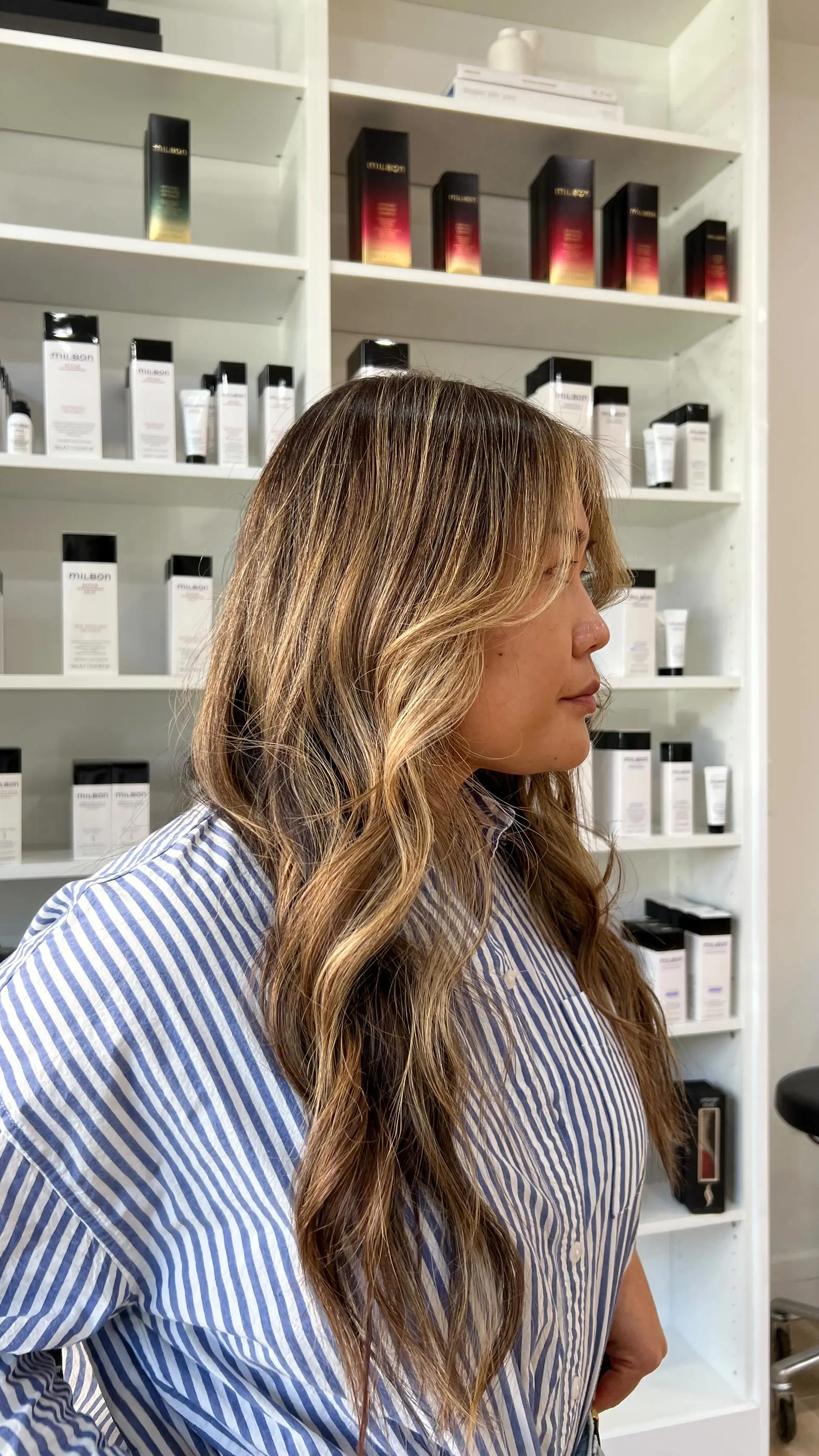 Long hair styled in loose dimensional waves featuring warm honey blonde balayage and soft face-framing curtain layers. 1