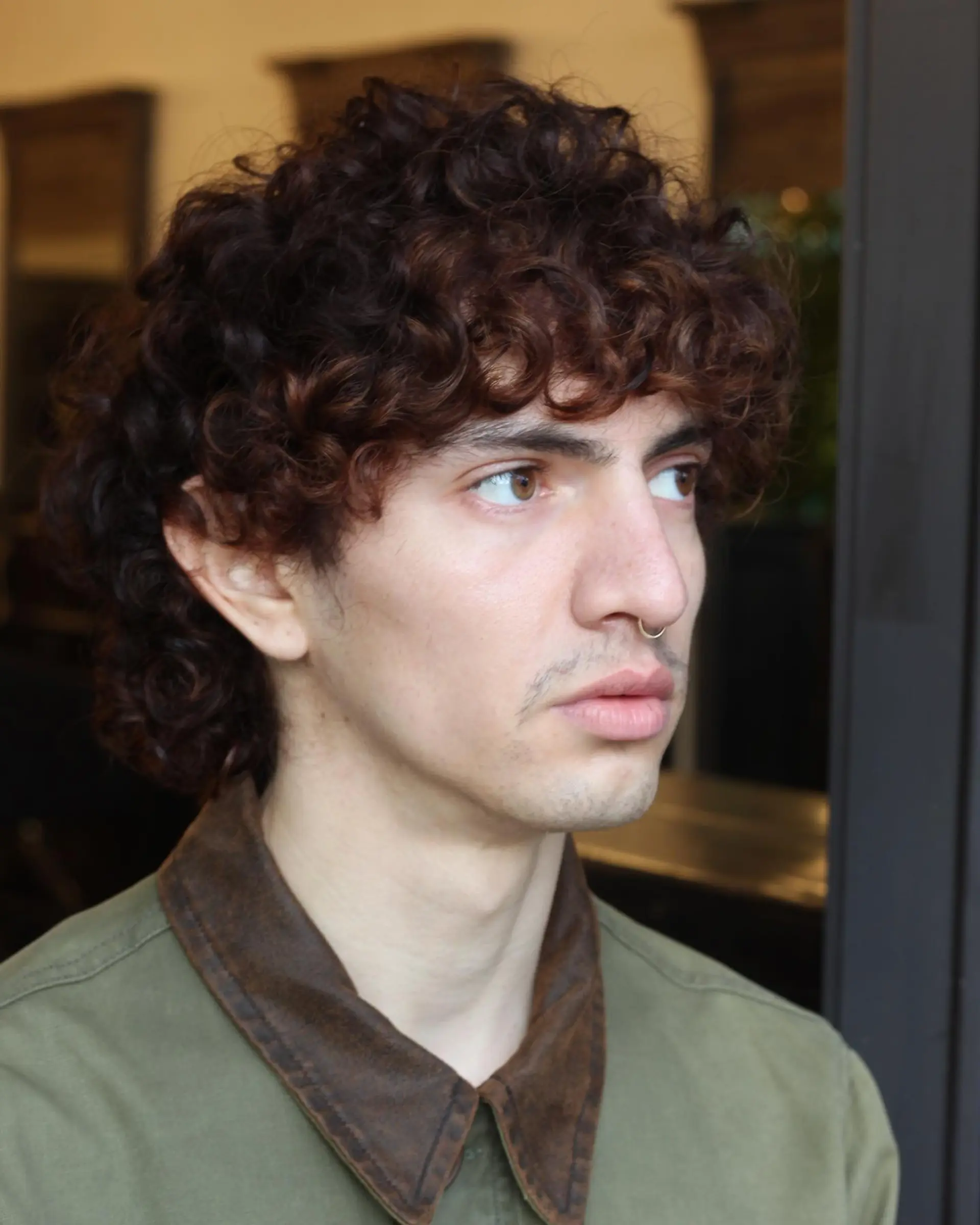 A defined curly modern mullet featuring textured curls with a forward-falling fringe and extended length at the nape. 1