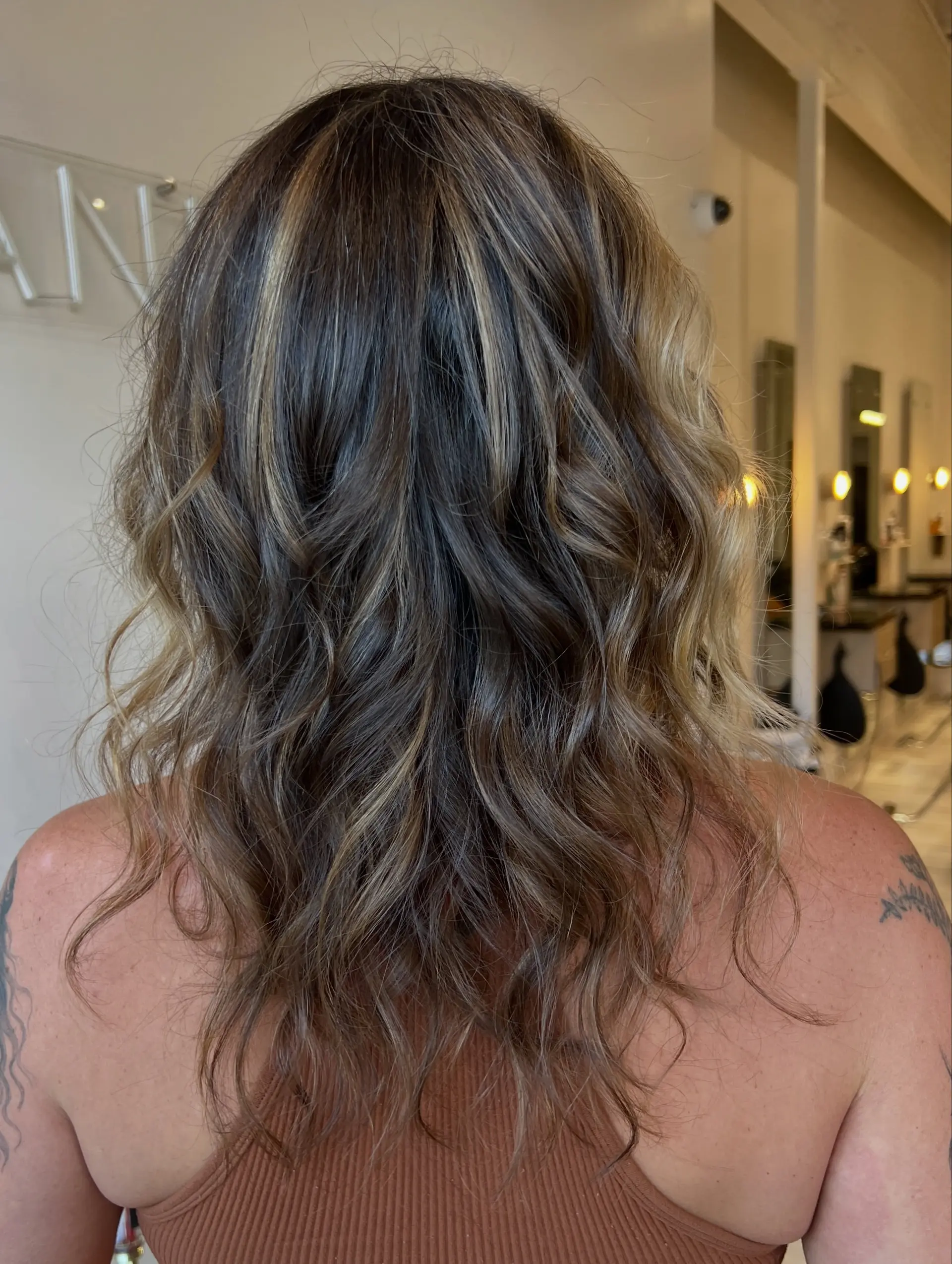 Medium-length brunette hair featuring blended caramel and golden blonde highlights, styled into loose, textured waves. 1