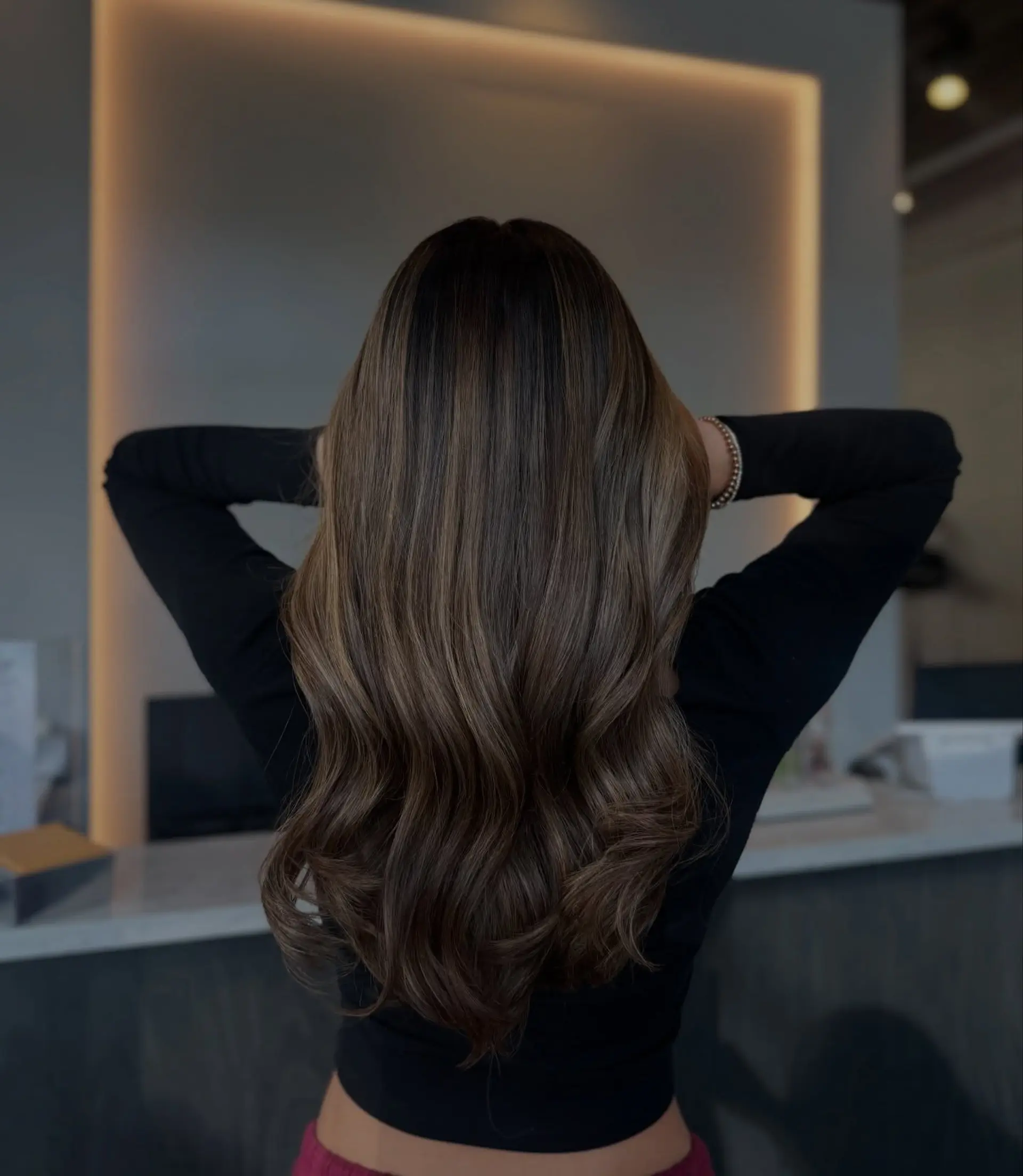 Long, flowing warm brunette hair with blended caramel foilyage highlights styled into smooth waves. 1