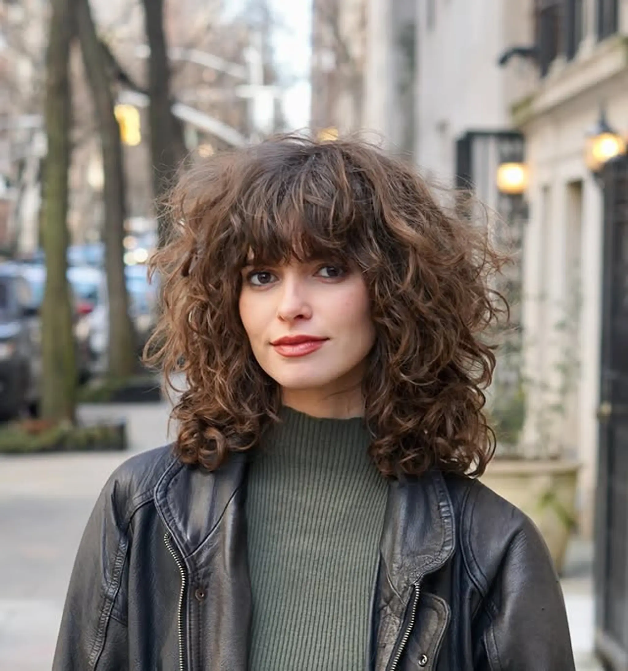 This shaggy curly bob features lots of layers for volume and a carefree, retro-inspired look. The bangs add a playful touch to this naturally textured hairstyle.