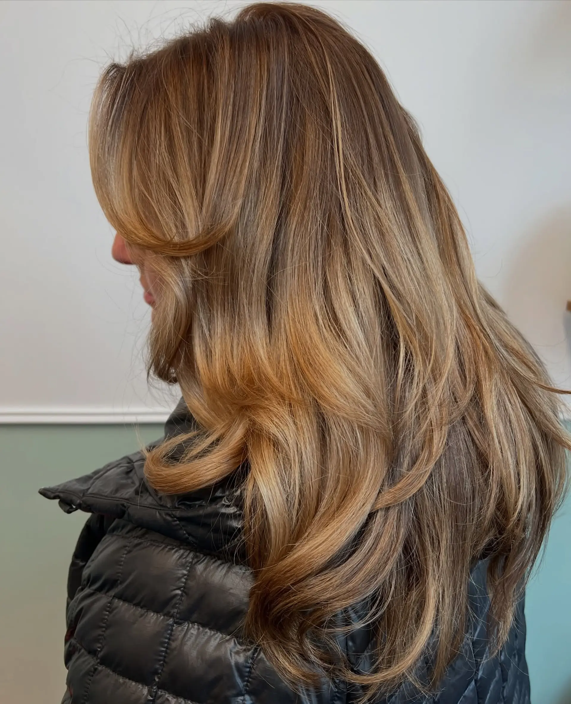 Long honey-blonde balayage featuring blended golden highlights and feathered face-framing layers styled in a soft blowout. 1
