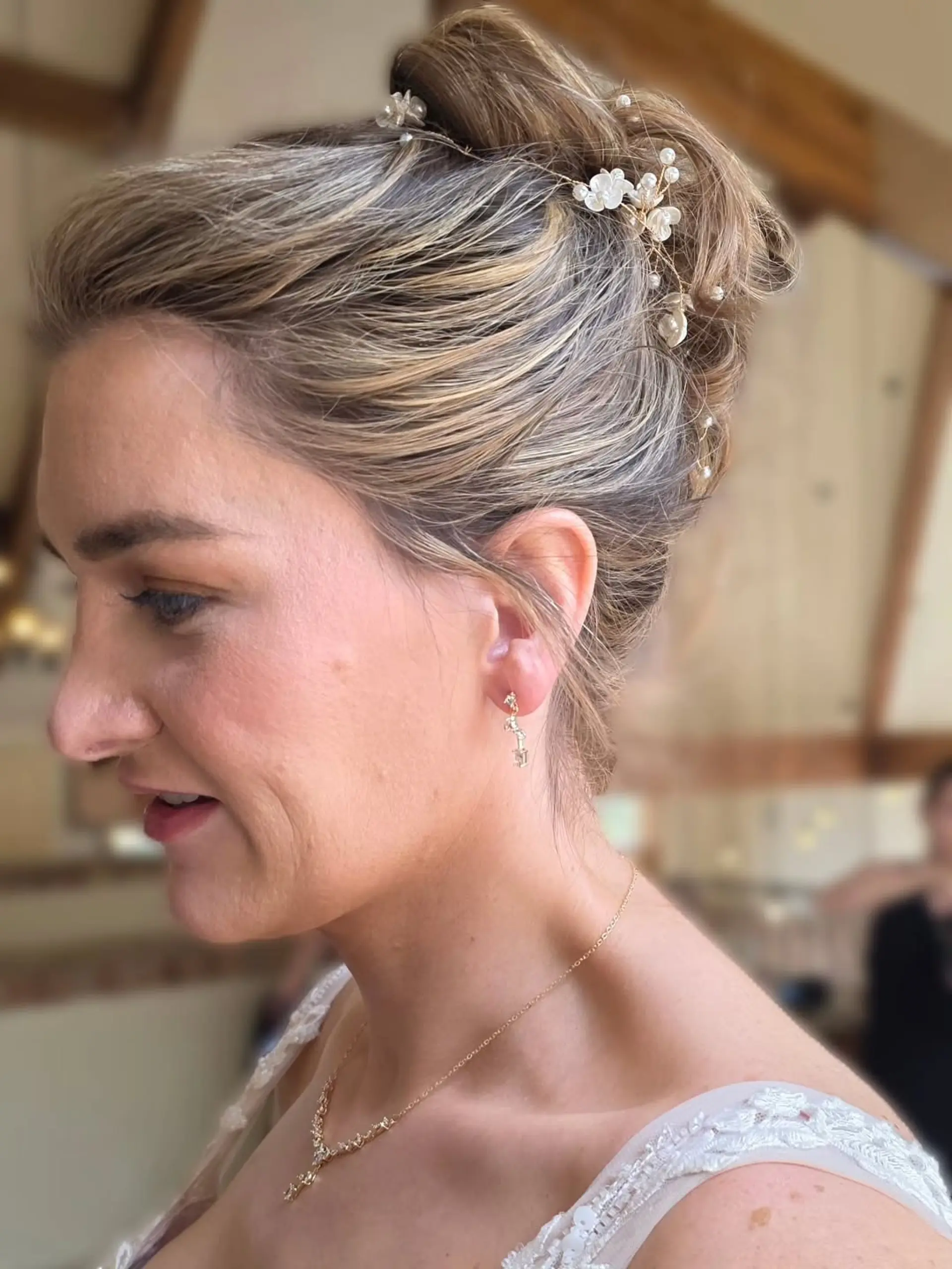 An elegant bridal high updo featuring swept-back dimension and adorned with delicate pearl and floral hair accessories. 1
