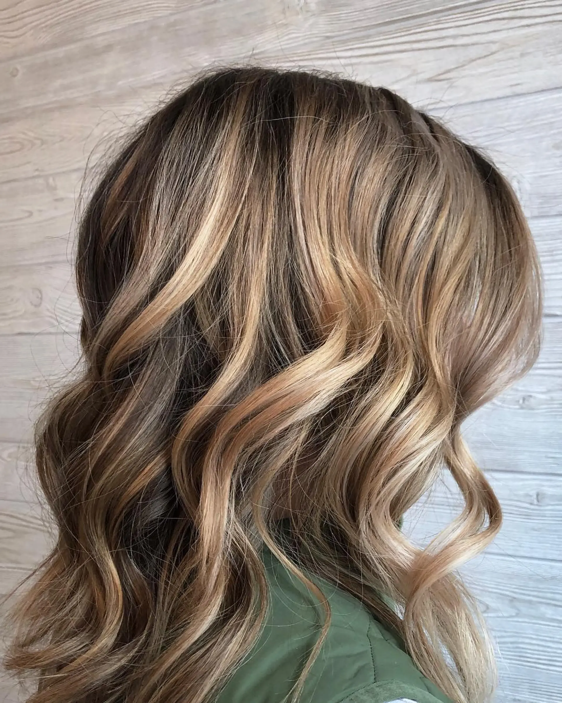 Medium-length dimensional balayage featuring warm caramel and honey blonde tones blended into a brunette base, styled in soft waves. 1