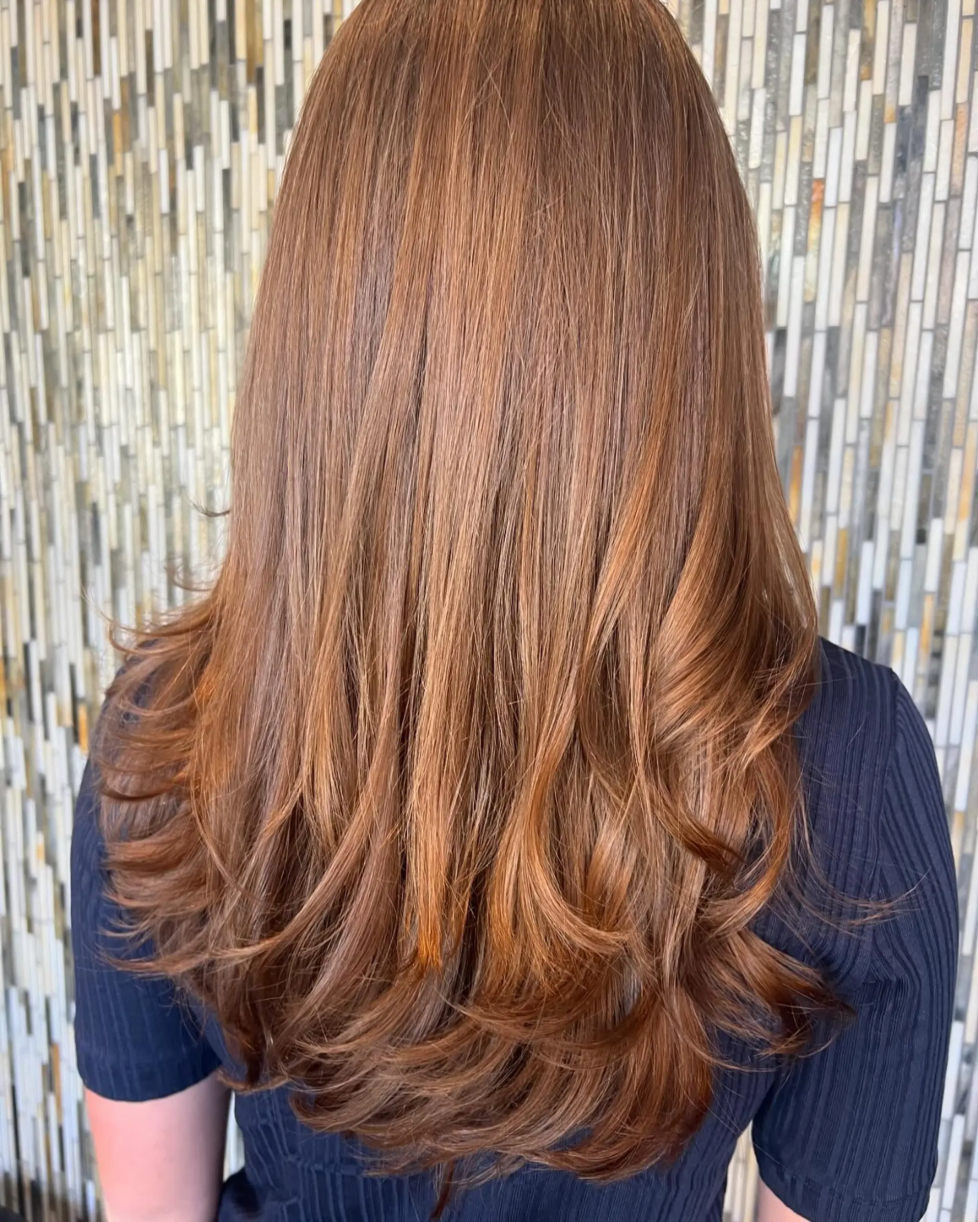Long, warm auburn hair featuring soft cascading layers and turned-in flipped ends from a blowout. 1