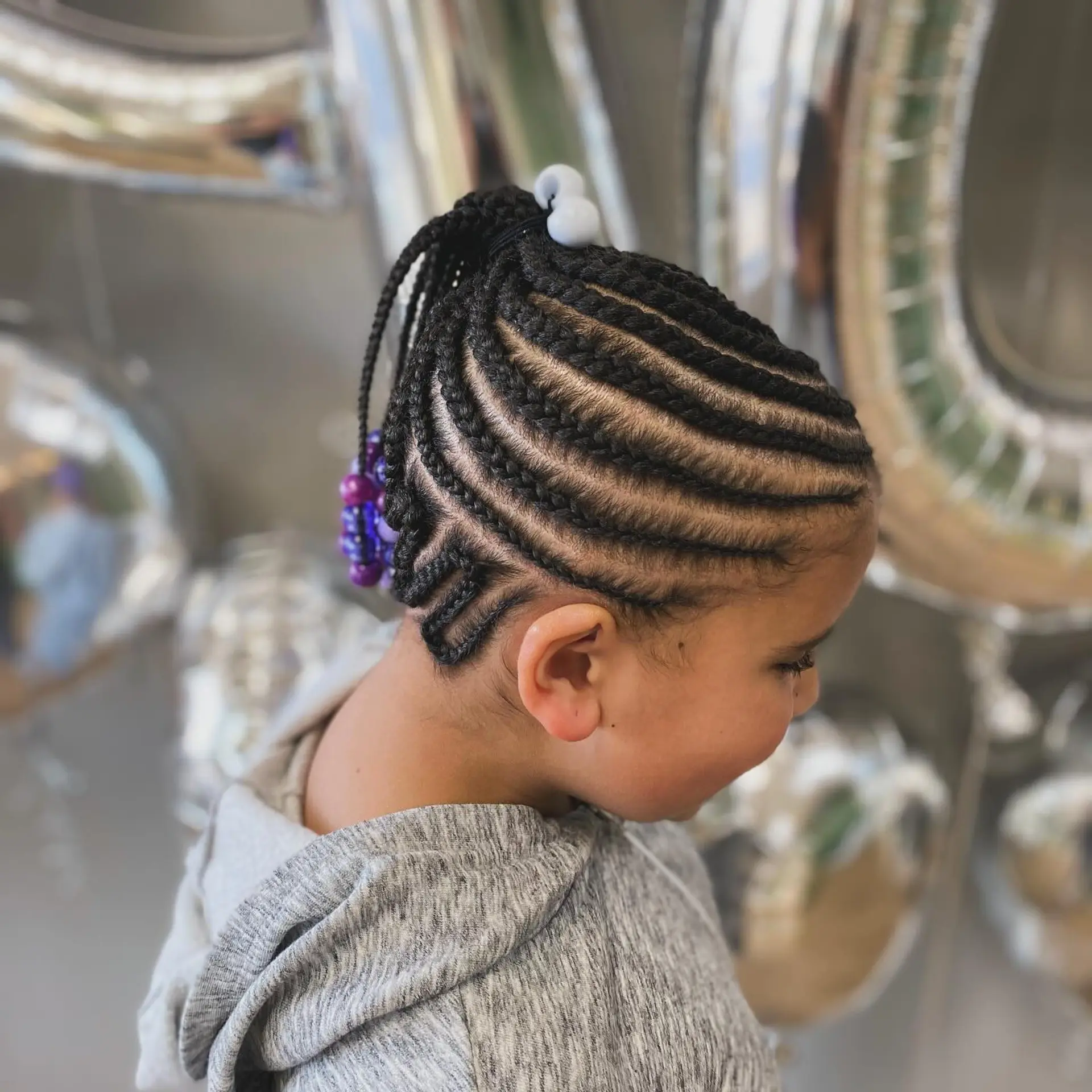 Clean, curved cornrows styled into a high ponytail adorned with colorful beads. 1
