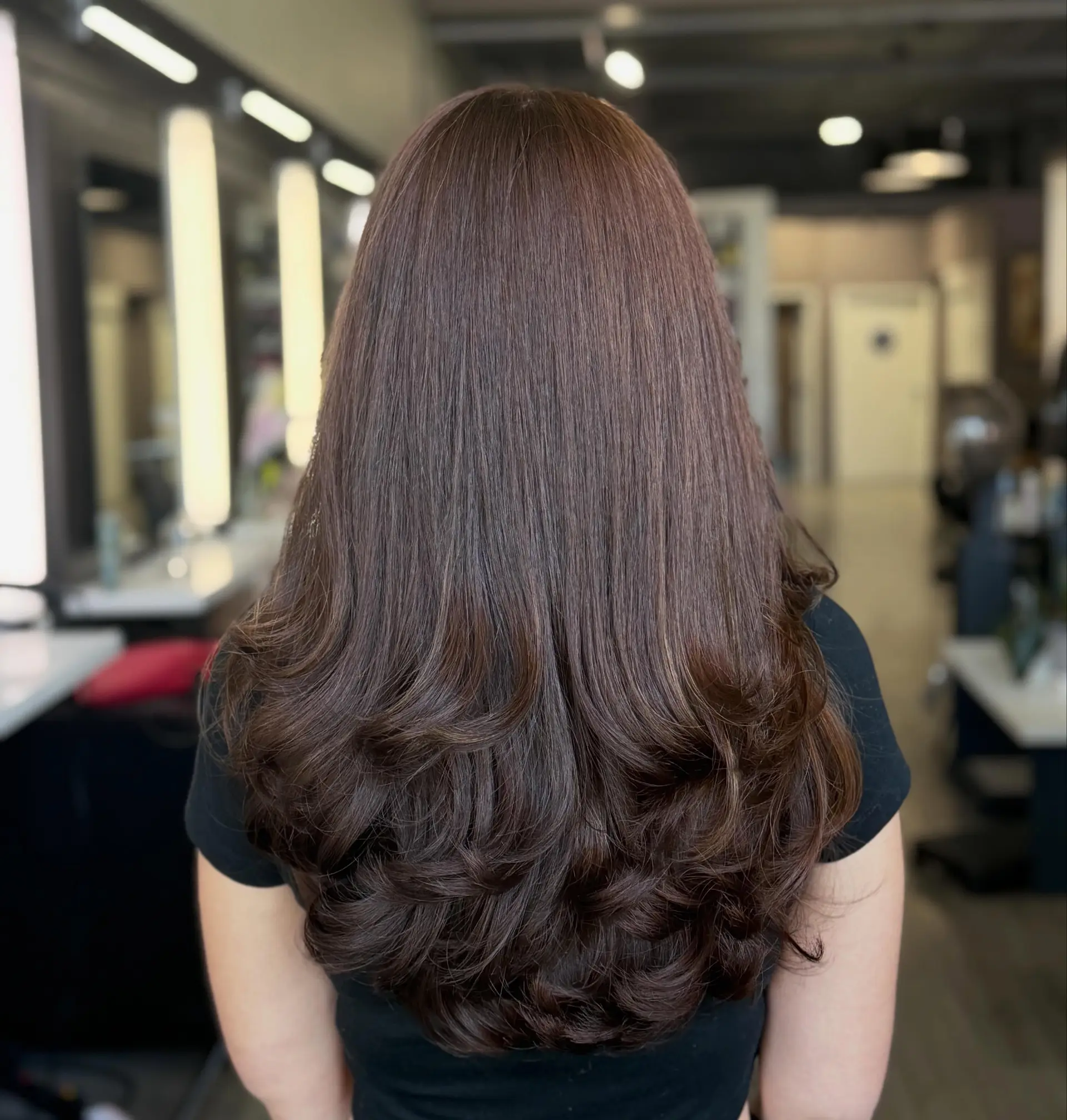 Long chocolate brown hair styled into cascading blowout layers with bouncy curled ends. 1