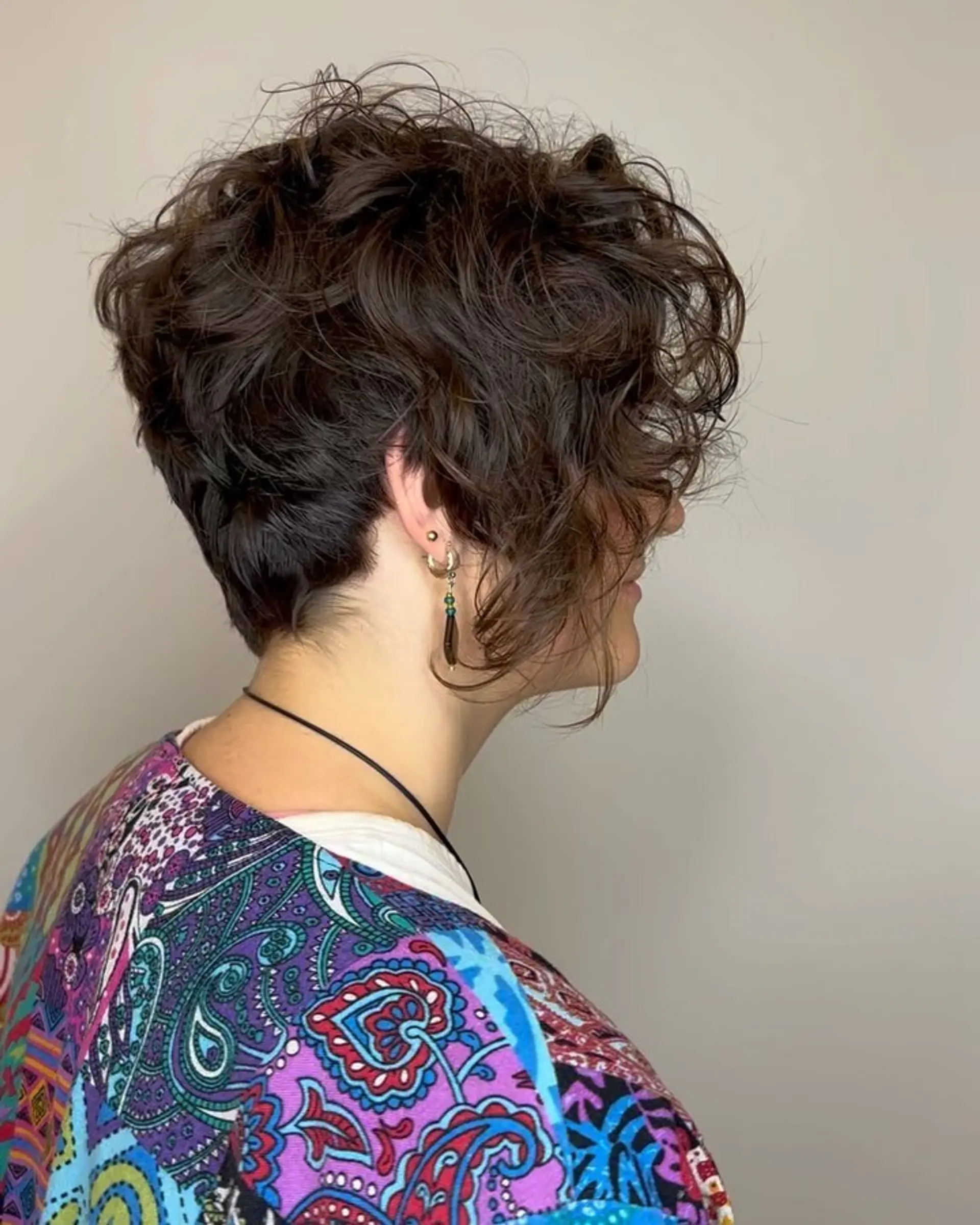 A textured curly pixie cut featuring a tapered nape and voluminous, tousled curls layered across the crown and framing the face. 1