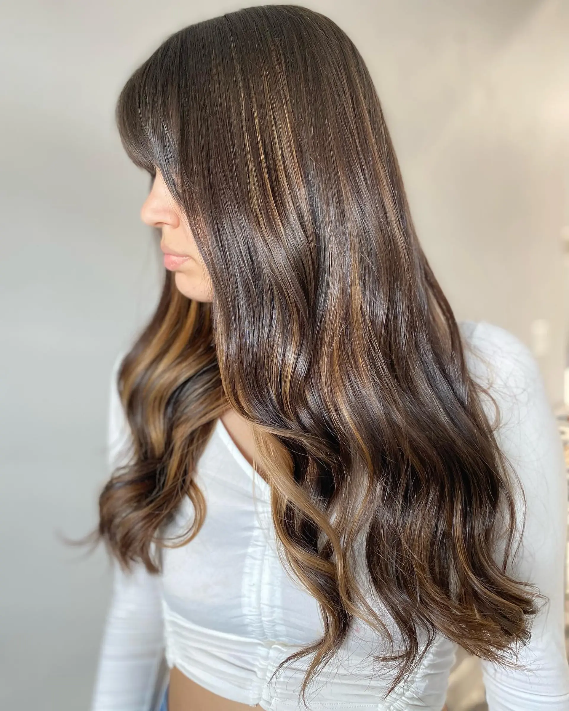 A long wavy hairstyle with face-framing blonde highlights and trendy curtain bangs. 1