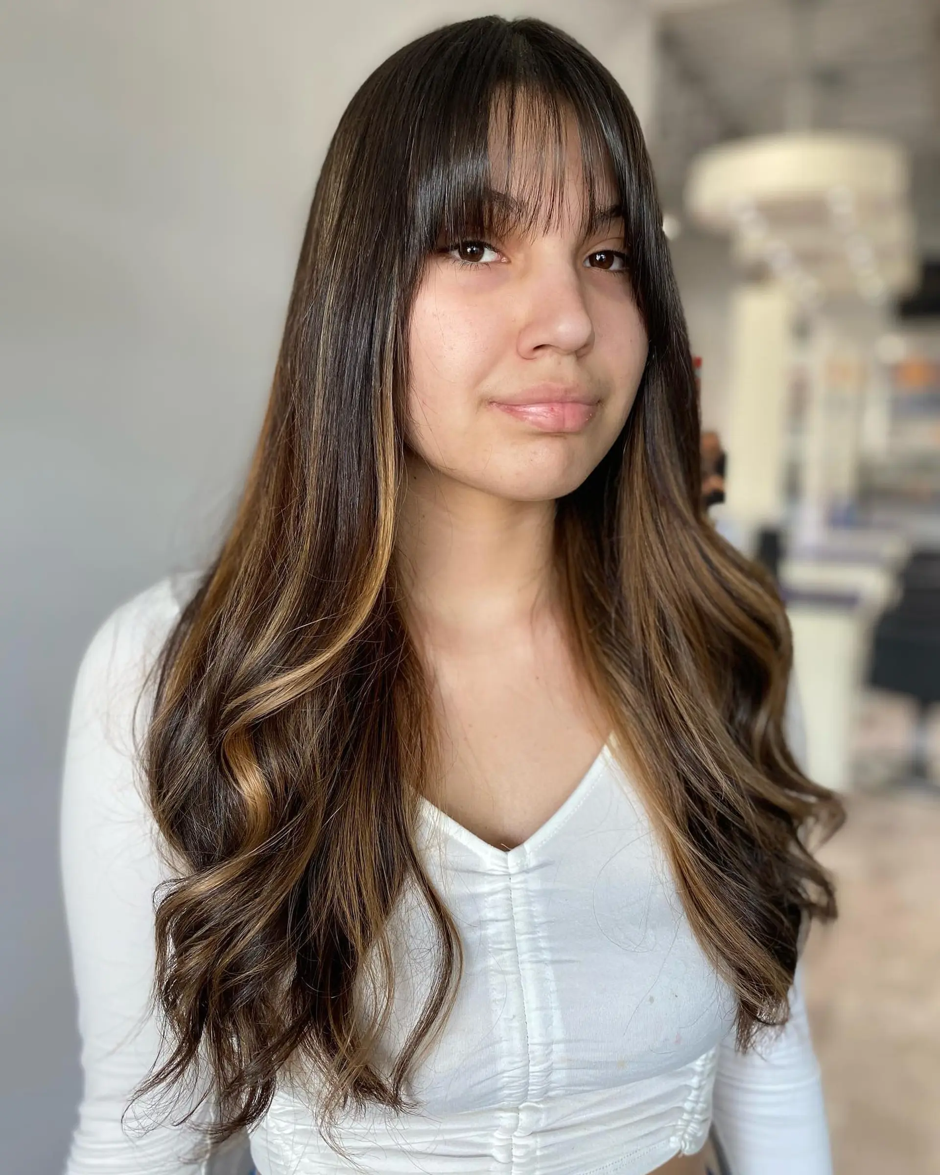 A long wavy hairstyle with face-framing blonde highlights and trendy curtain bangs. 3