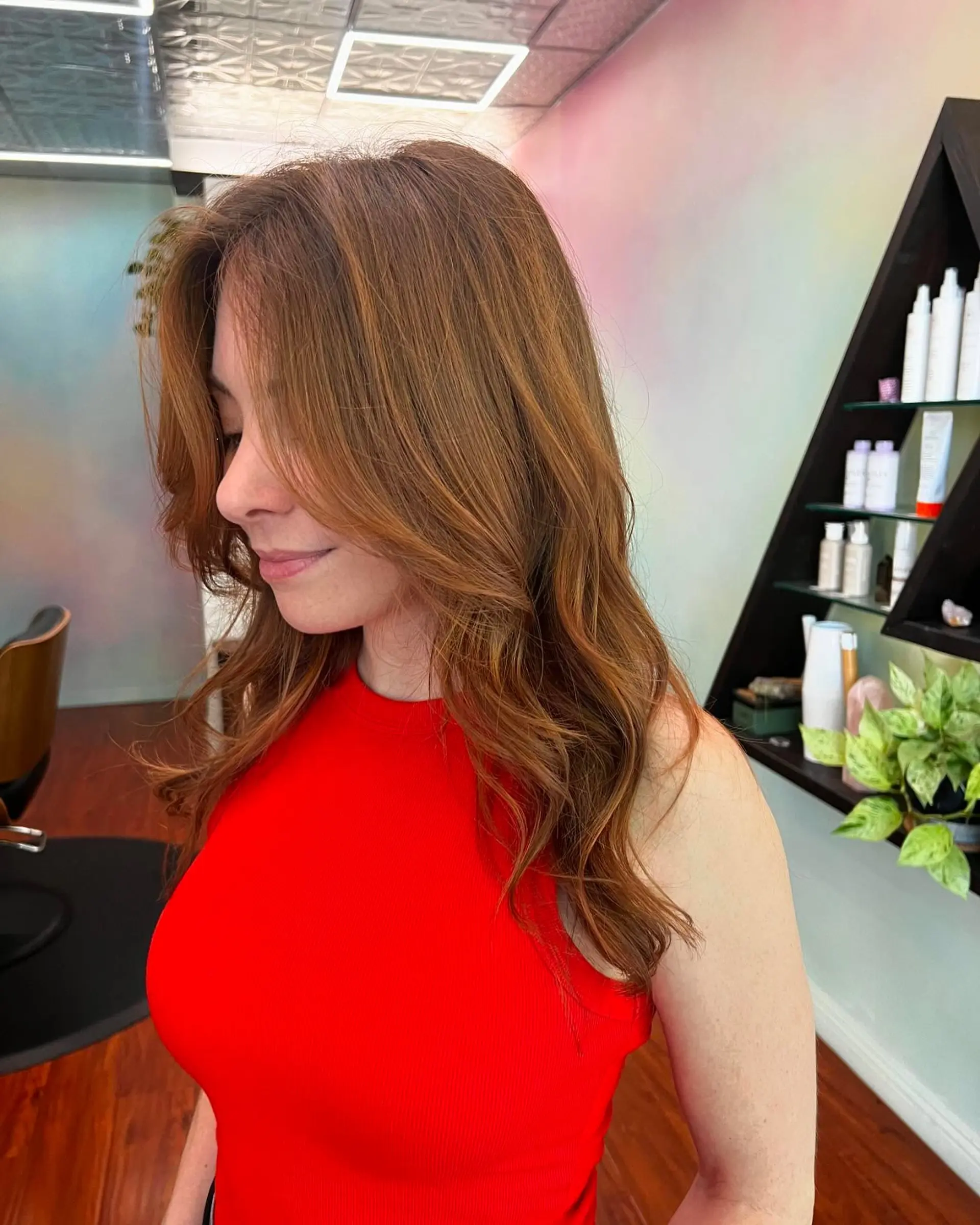 Long warm auburn hair cut with soft, face-framing layers and styled into gentle loose waves with natural dimensional highlights. 1