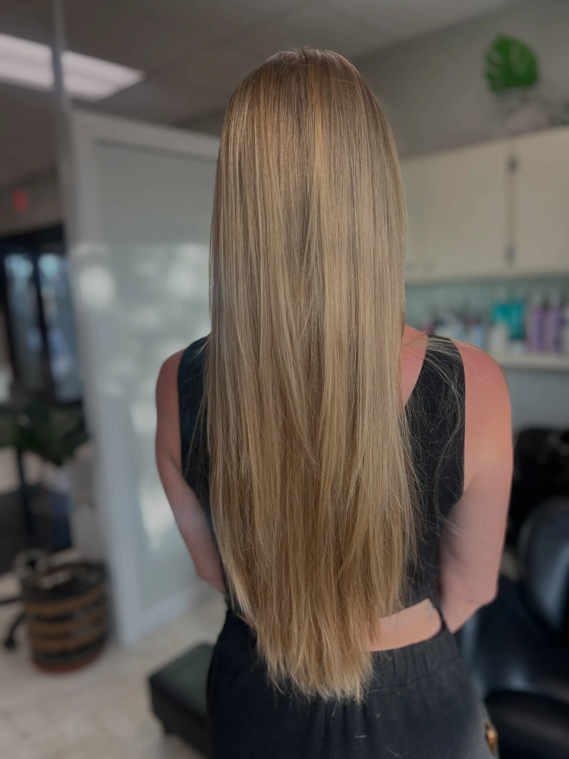 Extra-long, straight warm blonde hair cut with flowing blended layers and styled smooth. 1