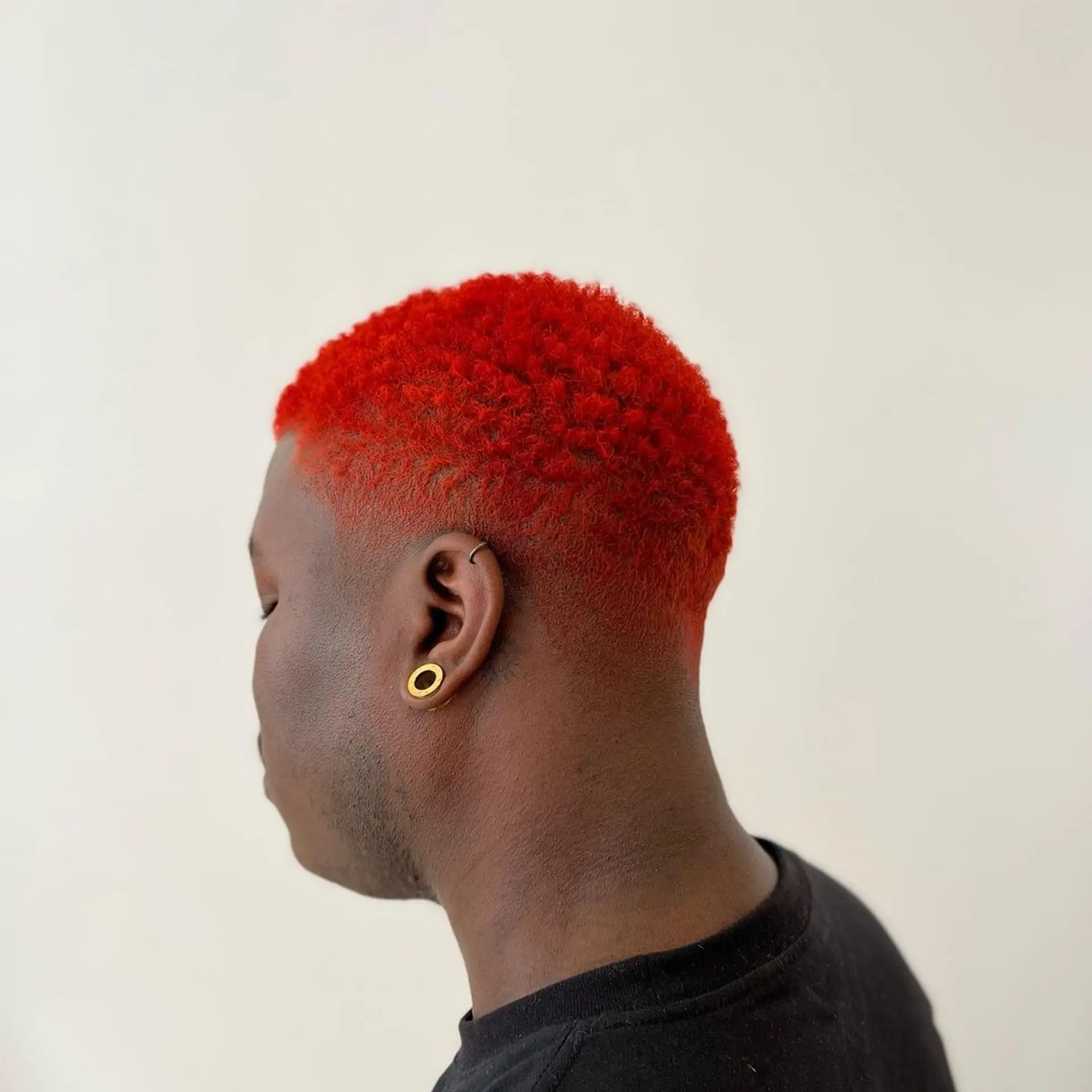 Short, curly hair dyed red with a distinct fade on the sides and back, cut evenly and closely to the scalp. 2