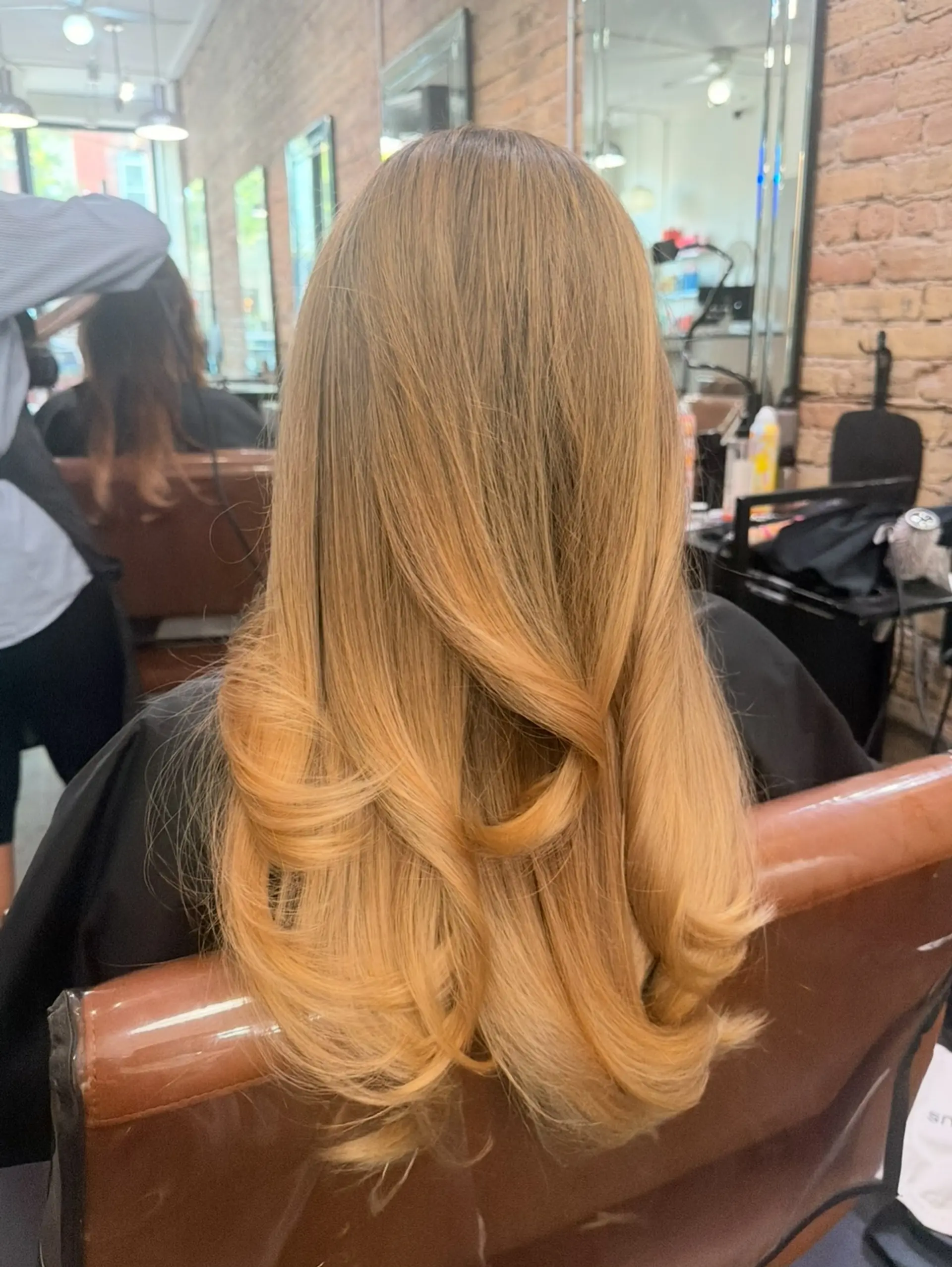 Long warm honey-blonde hair styled in a bouncy blowout with layered flipped ends. 1